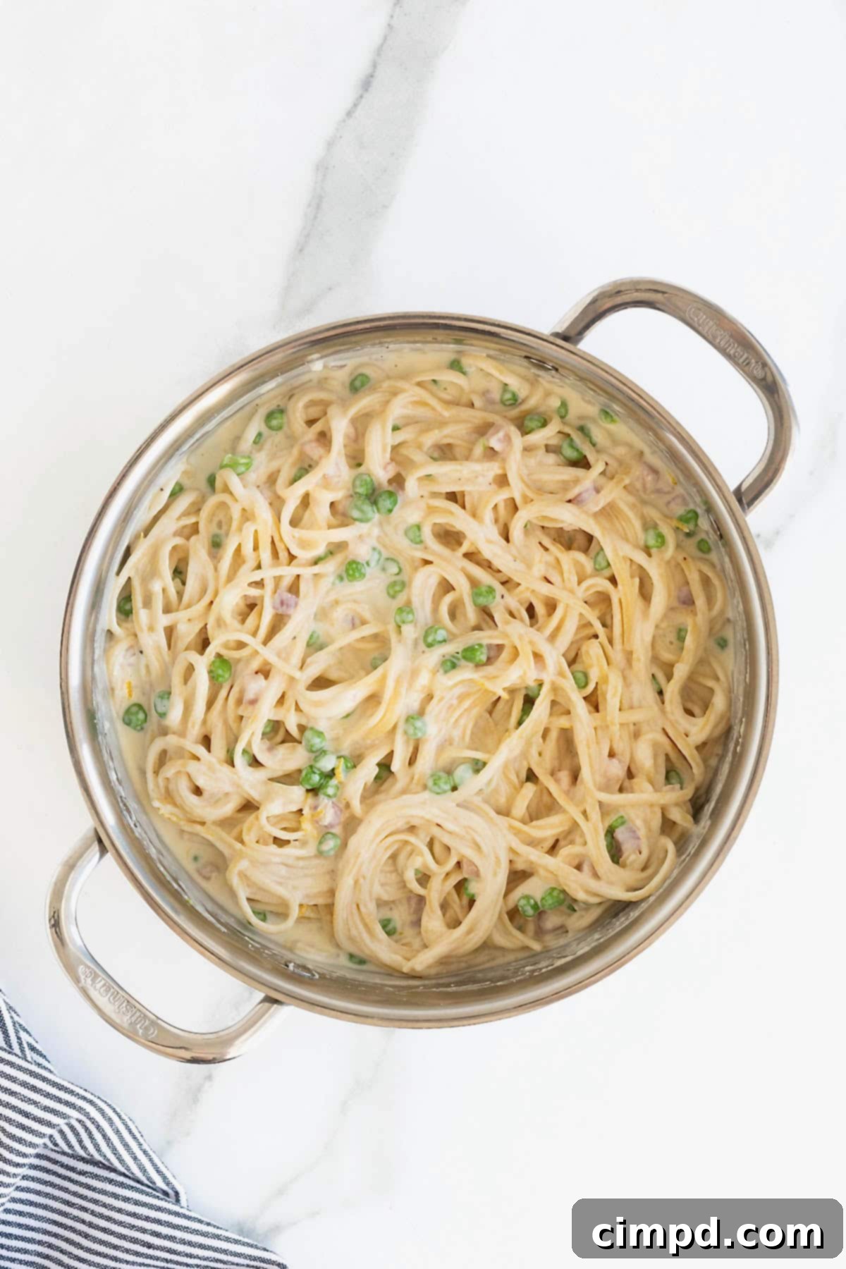 Linguini fully coated in a creamy white sauce, nestled in a stainless steel pot, ready to be served.