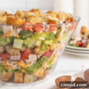 Club Salad Parfait 13 A large clear glass salad bowl filled with layers of croutons, salad mix, shredded cheese, bacon, ham and tomatoes.