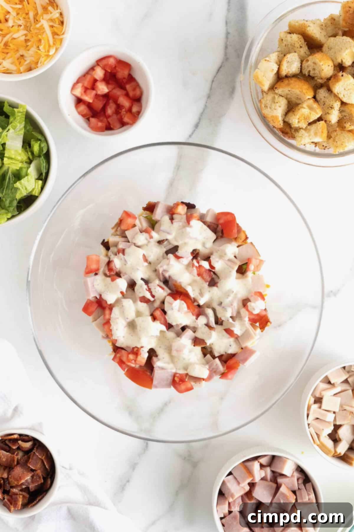 Club Salad Parfait 9 Dressing drizzled on top of a club salad in a clear glass salad bowl on a white marble counter.