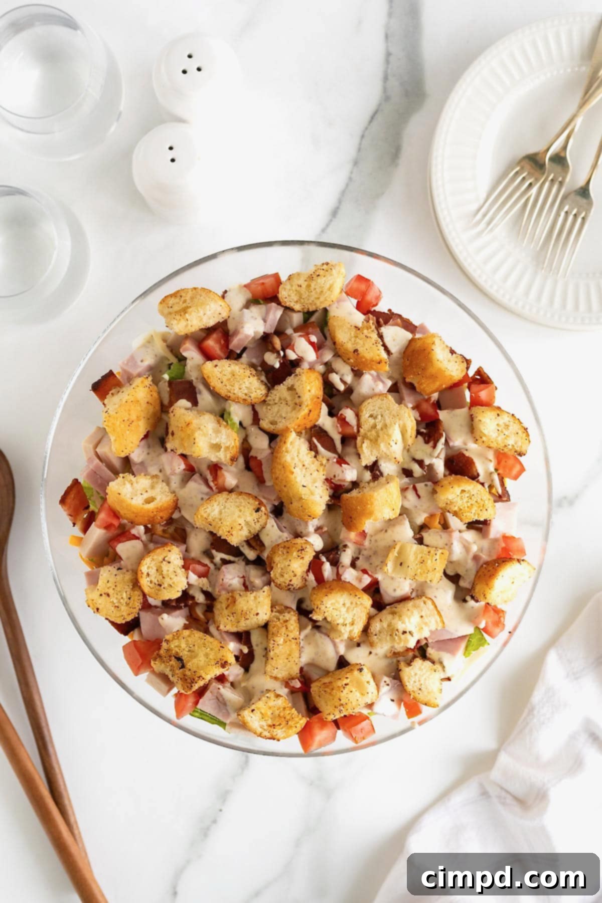 Club Salad Parfait 10 Croutons on top of a club salad in a large glass salad bowl on a white marble counter.