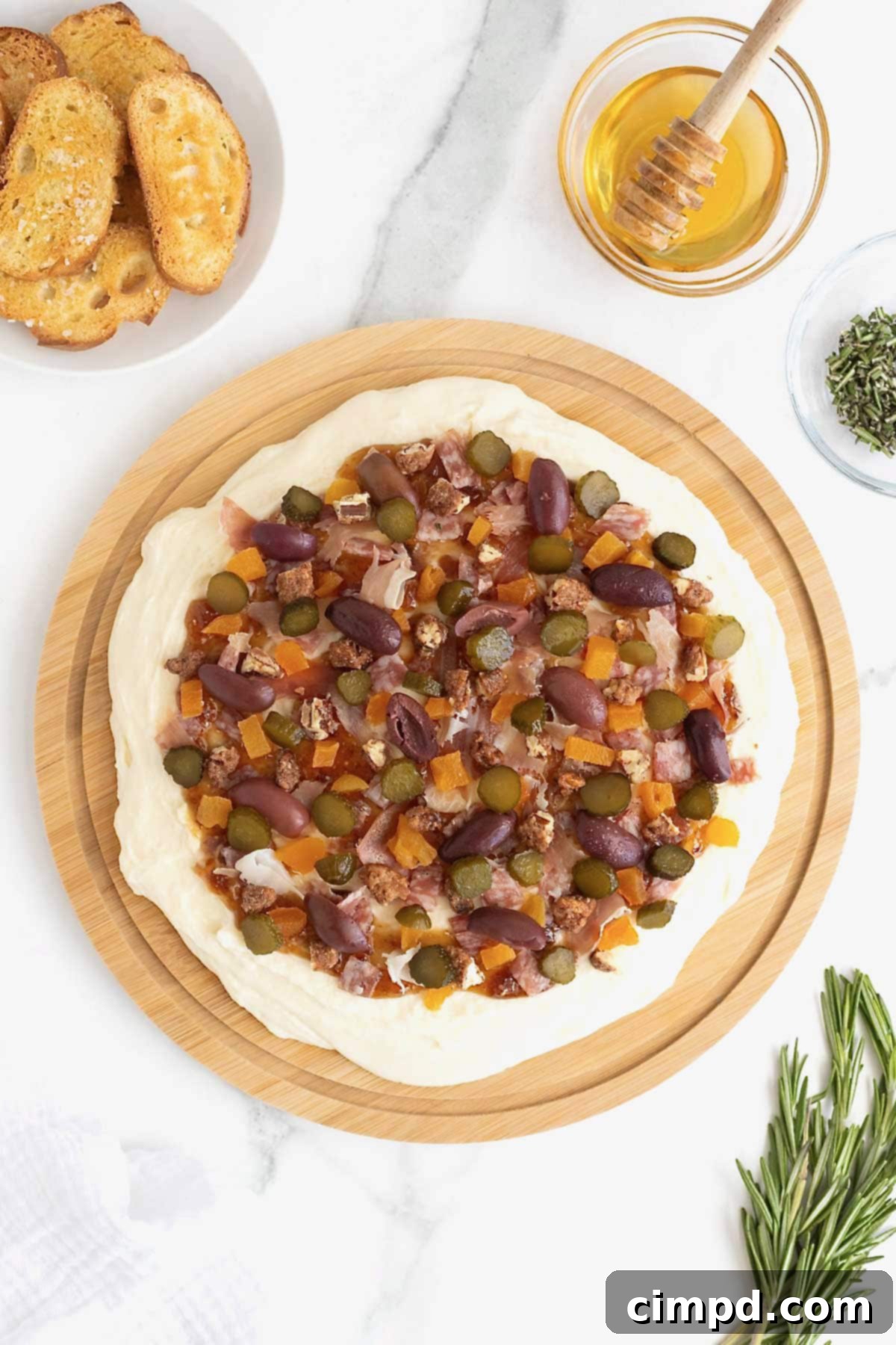 A close-up of the charcuterie dip as savory prosciutto, salami, olives, and crunchy pecans are artfully sprinkled over the fig-swirled whipped brie.