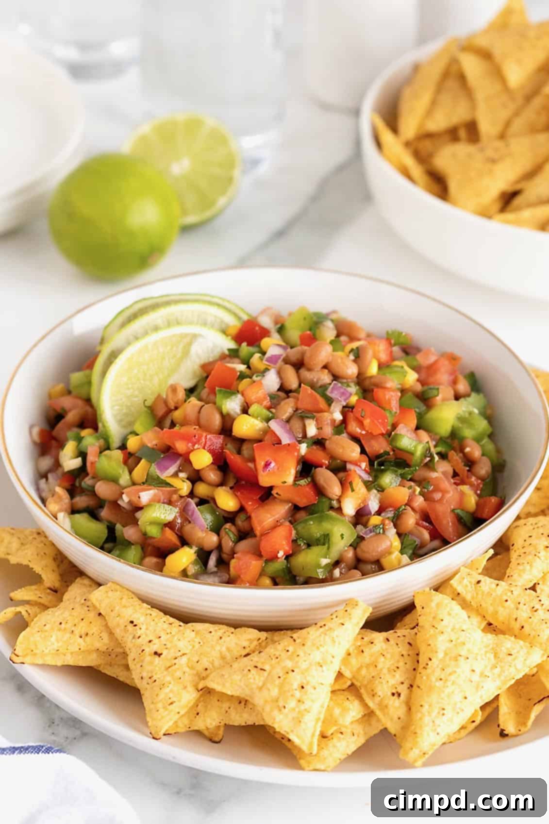 A large gold-rimmed white serving bowl of Baked Bean Cowboy Caviar, garnished with two fresh lime slices, ready for serving at a party.