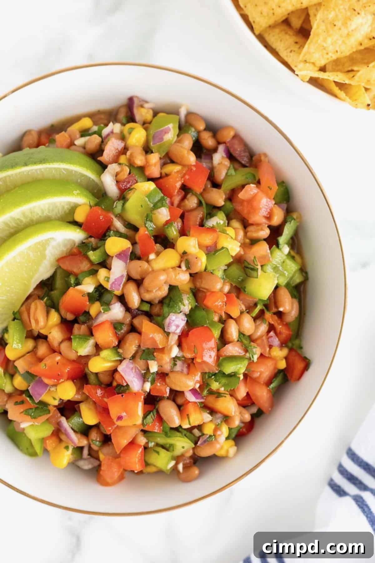 A large gold-rimmed white bowl filled with a colorful and fresh Baked Bean Cowboy Caviar, showcasing the vibrant ingredients.