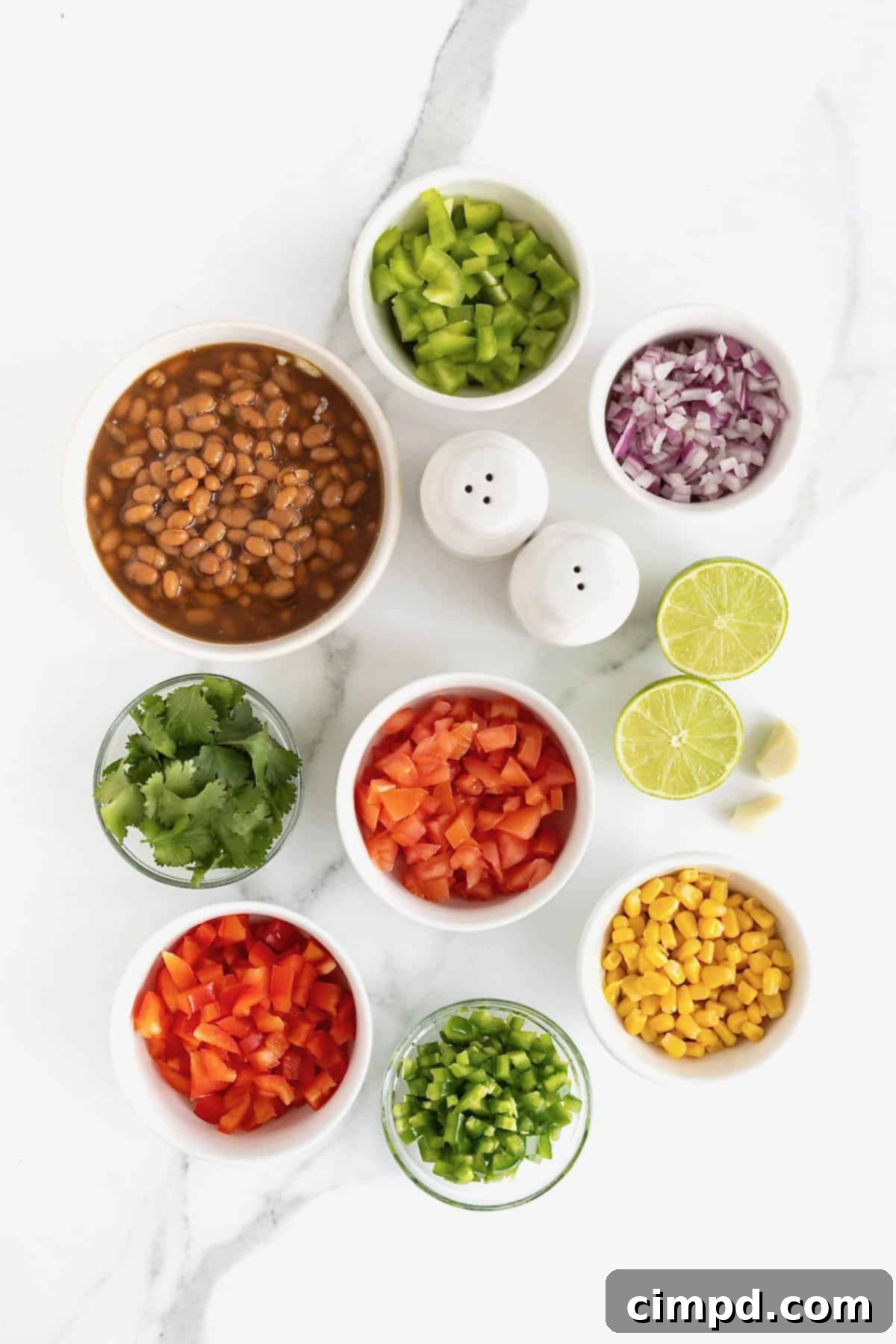 A neatly arranged collection of fresh ingredients for Baked Bean Cowboy Caviar, displayed in small white dishes on a elegant white marble countertop, highlighting the recipe's freshness.