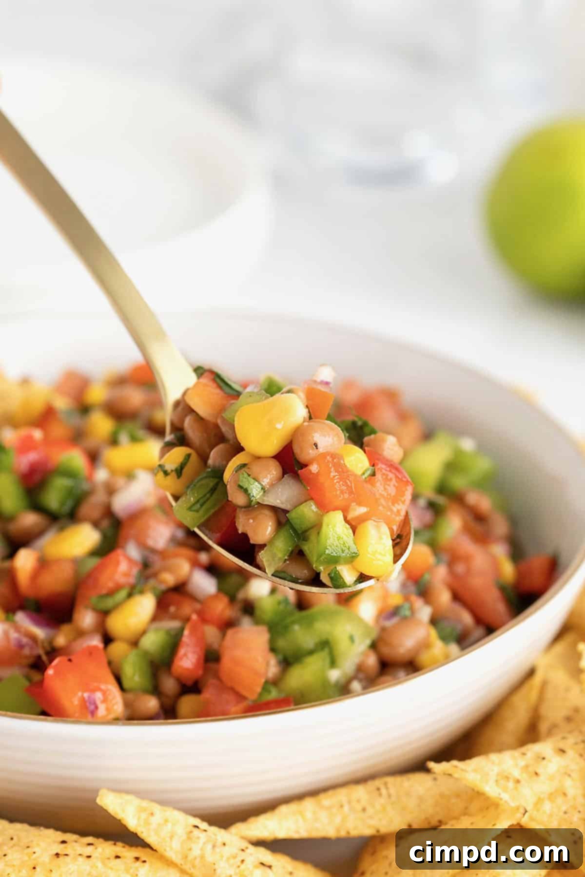 A spoon overflowing with Baked Bean Cowboy Caviar, held enticingly over a white bowl of the dip, showcasing its rich texture and colorful ingredients.