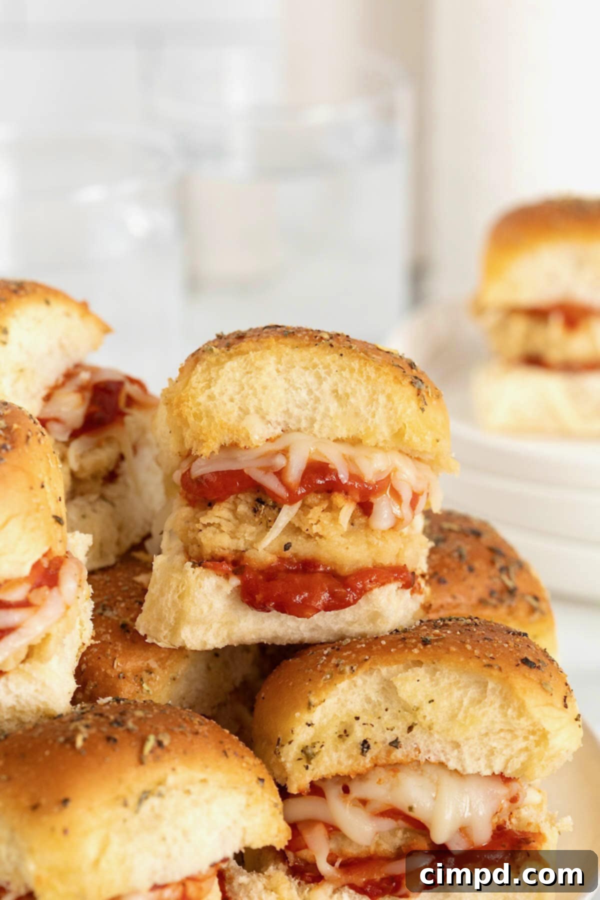 Golden brown chicken parmesan sliders on a wooden cutting board on a white marble counter, ready to be served.