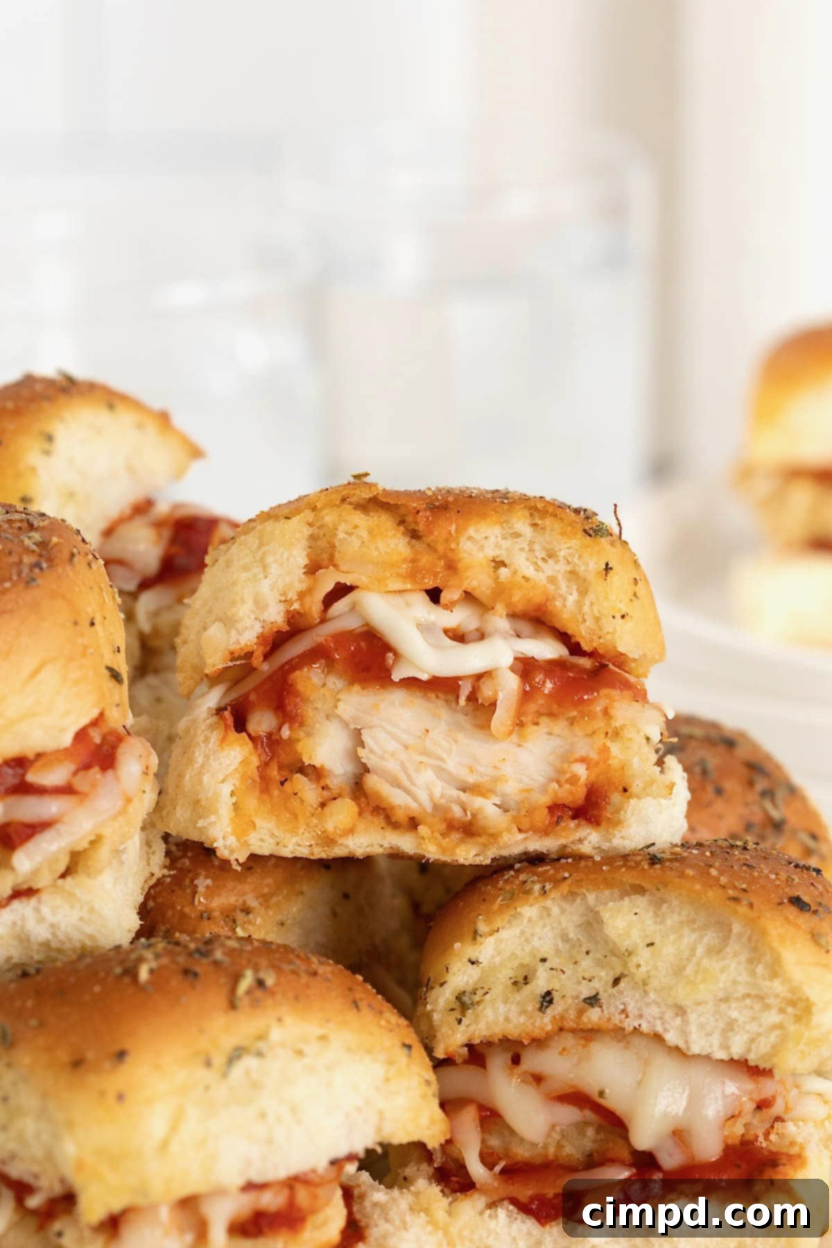 A close-up of stacked chicken parmesan sliders, one with a bite taken out, showing the melted cheese and chicken inside.
