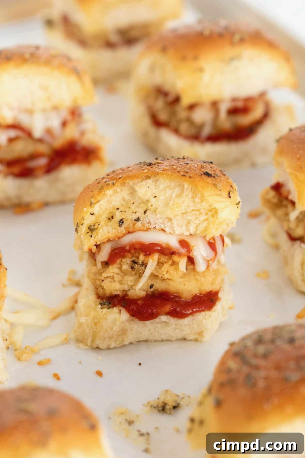 Chicken parmesan sliders arranged neatly on a parchment-lined baking sheet before baking.