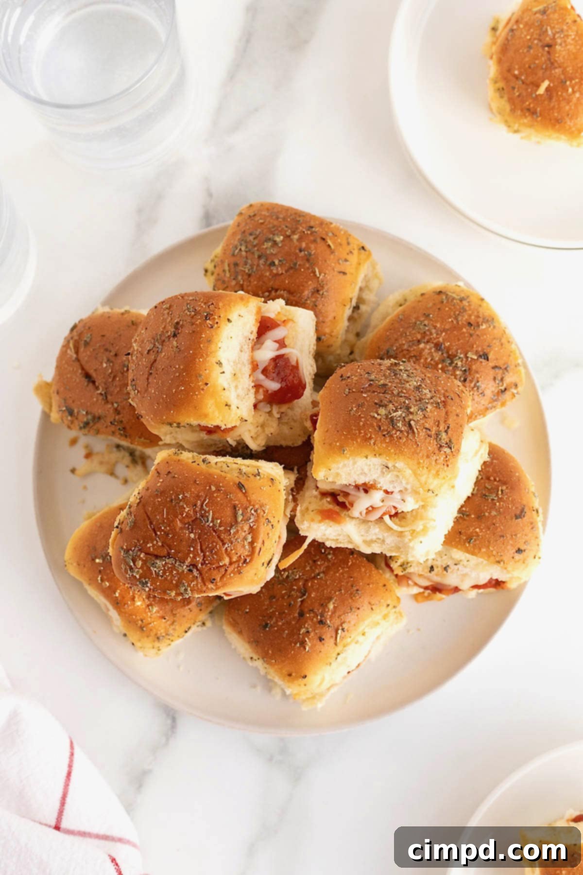 A large serving plate overflowing with hot, cheesy chicken parmesan sliders, garnished with fresh herbs.