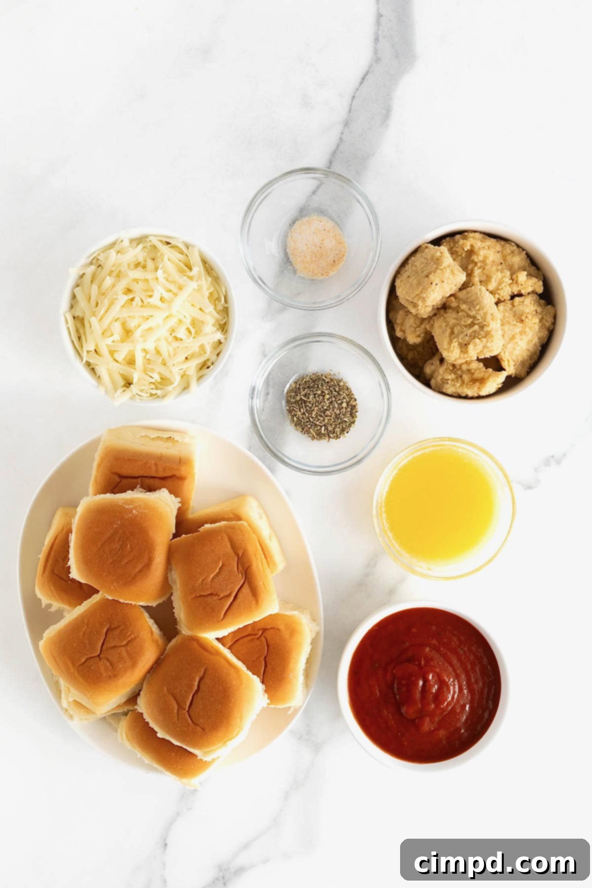 All the fresh and packaged ingredients laid out on a white marble counter, ready for making chicken parmesan sliders.