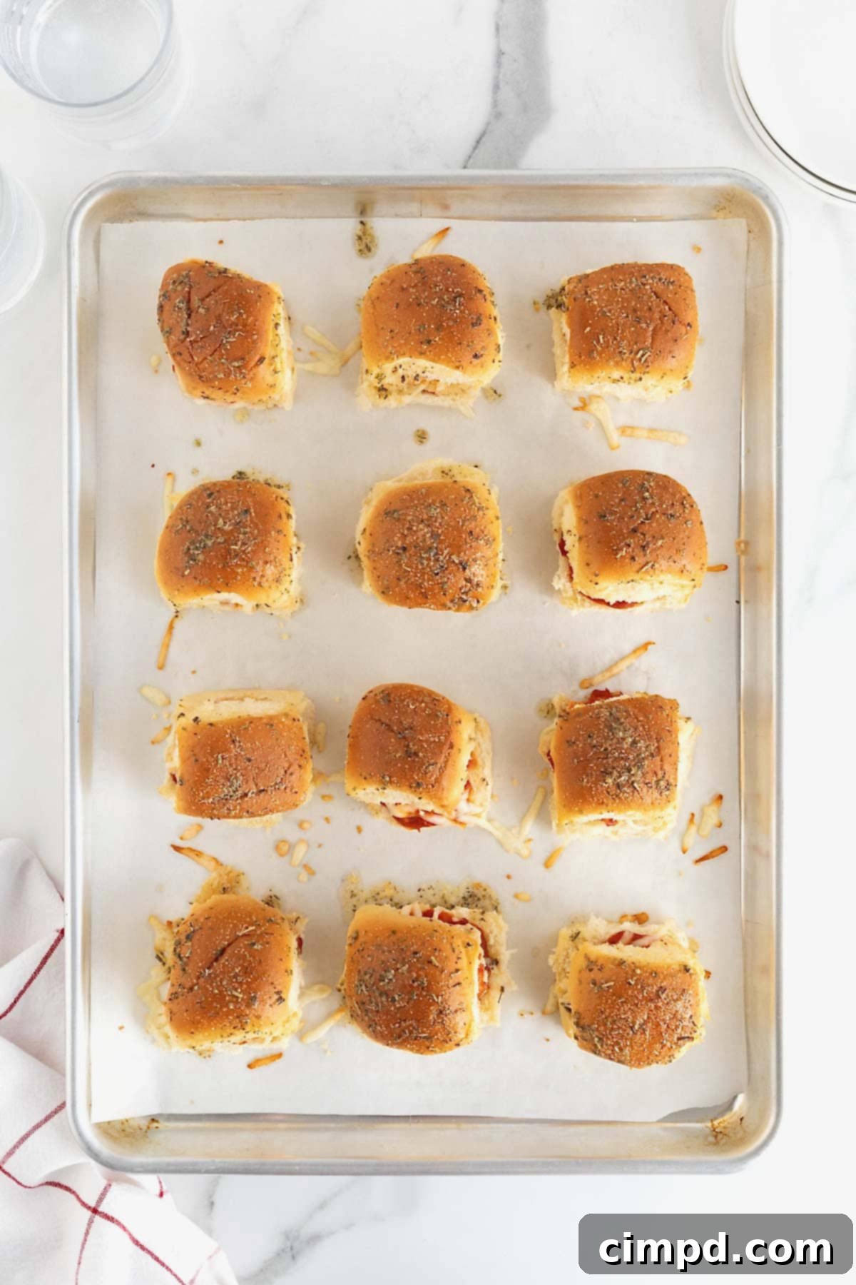 Twelve freshly baked chicken parmesan sliders, golden and cheesy, on a parchment-lined aluminum baking sheet.