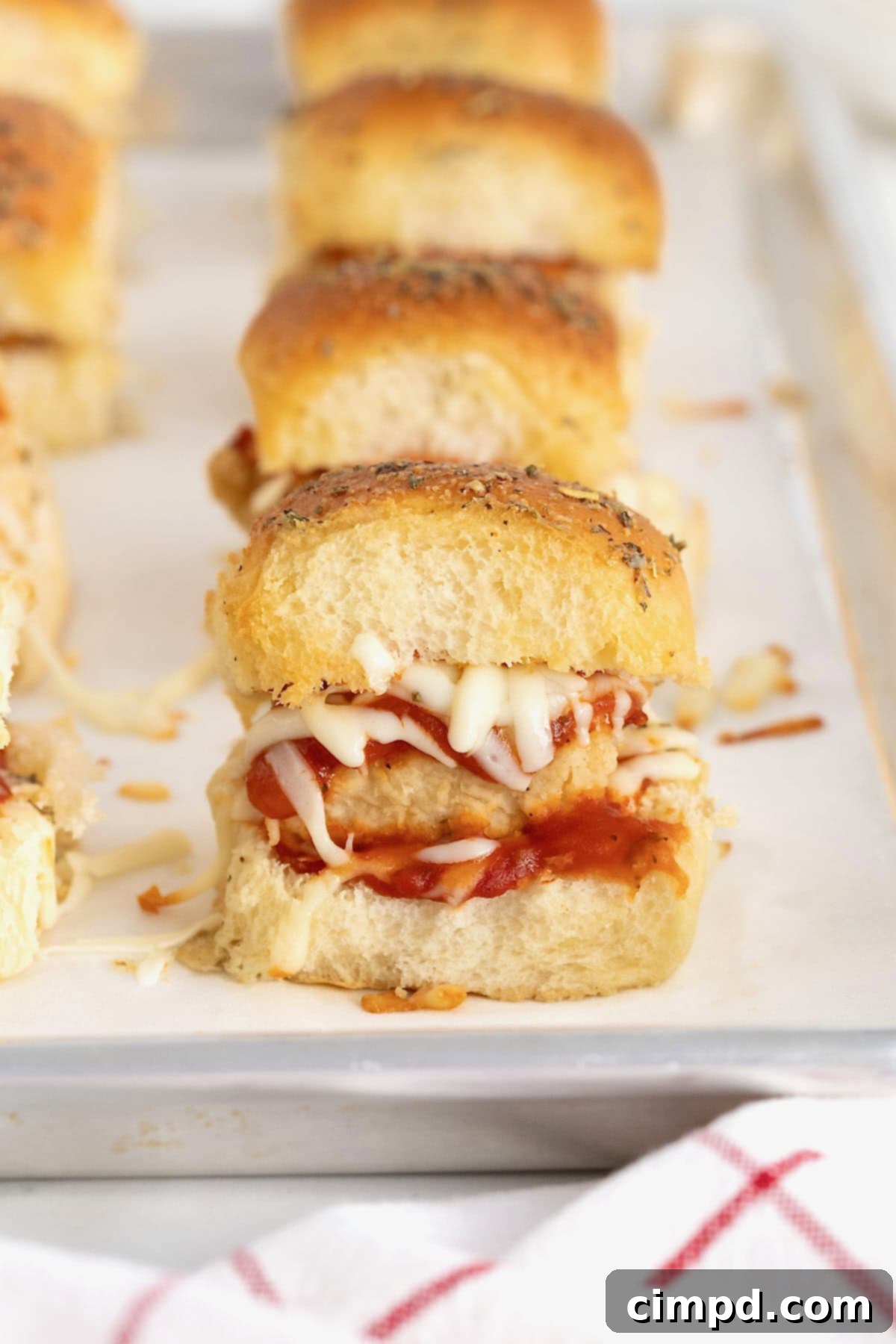A close-up of chicken parmesan sliders on a parchment-lined aluminum baking sheet, showing their delicious golden crust.