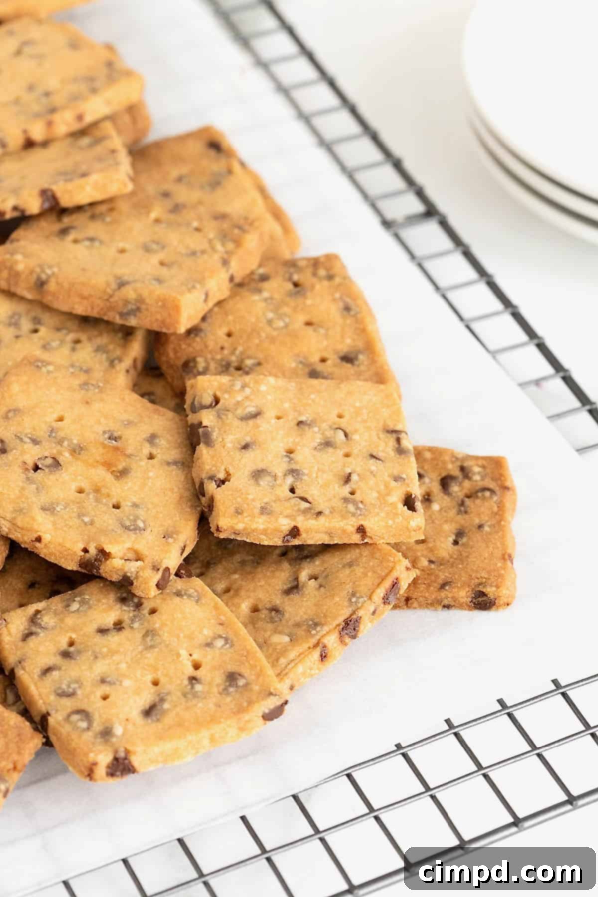 Crispy Chocolate Chip Snaps 11 A generous pile of freshly baked Chocolate Chip Cookie Crisps, glistening and golden, artfully arranged on a parchment-lined cooling rack.