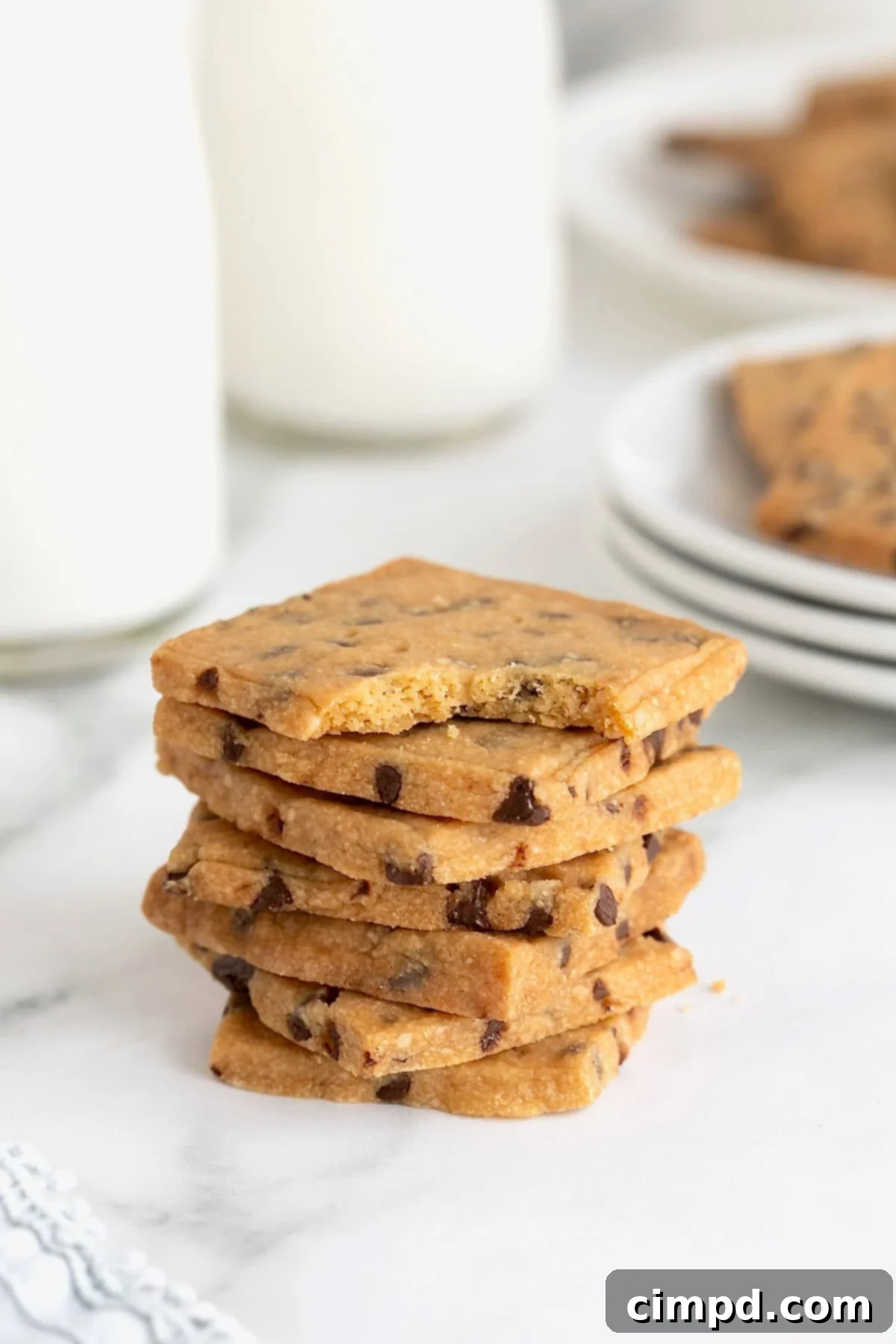 Crispy Chocolate Chip Snaps 3 A neat stack of seven golden chocolate chip cookie crisps arranged elegantly on a pristine white marble counter, highlighting their delicate texture.