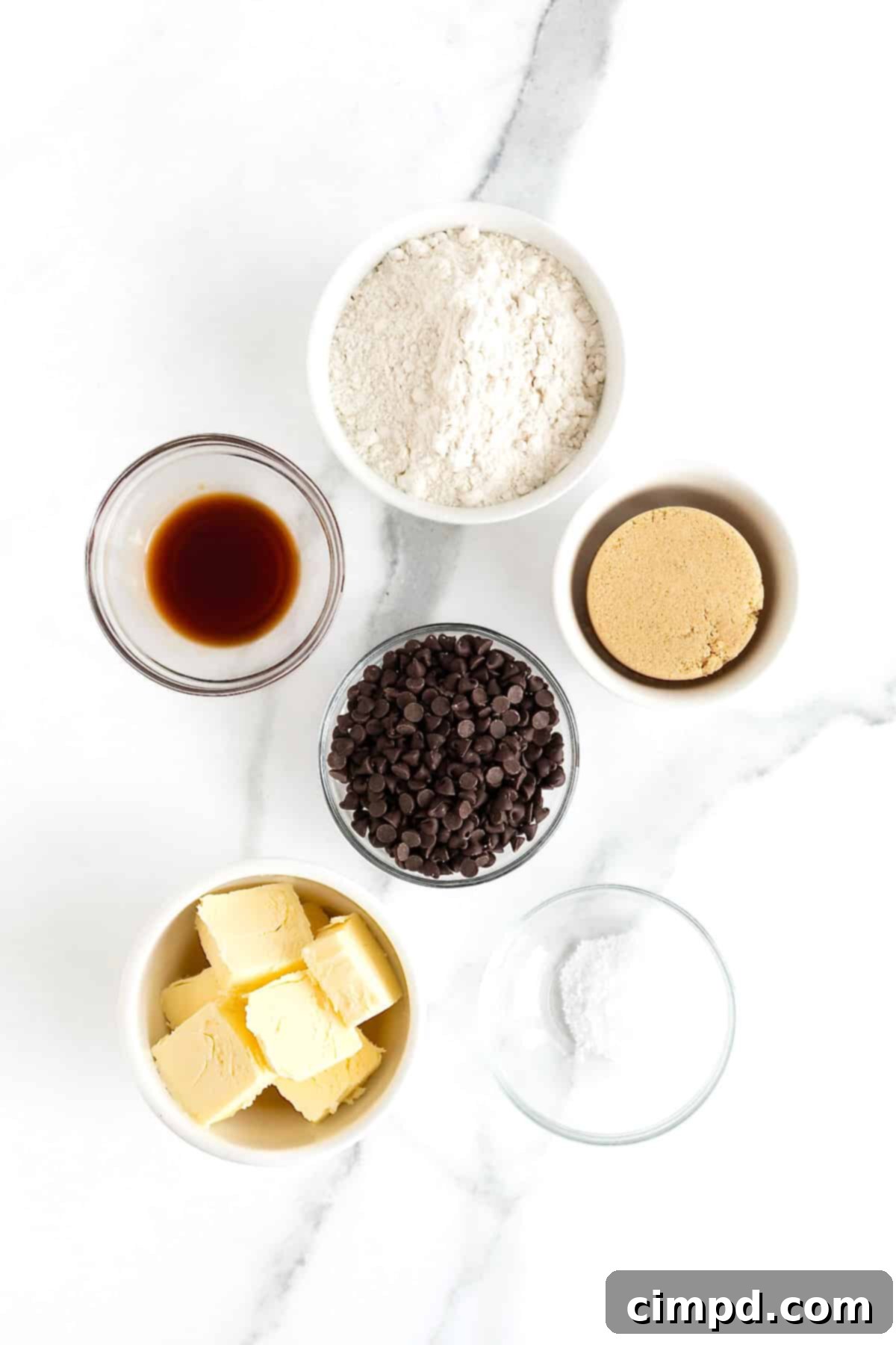 Crispy Chocolate Chip Snaps 5 An array of meticulously arranged ingredients for chocolate chip cookie crisps, displayed in small, elegant glass dishes on a sophisticated white marble counter.