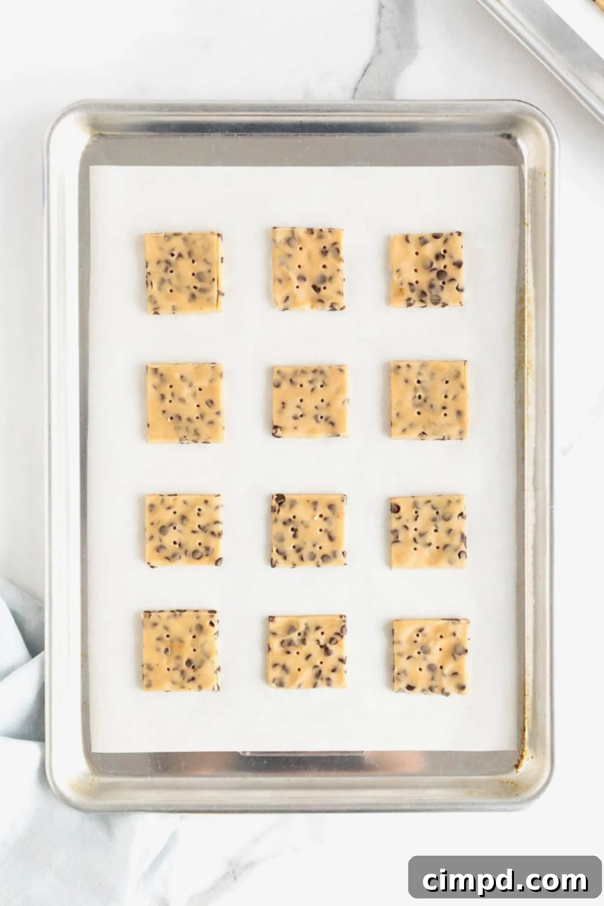 Crispy Chocolate Chip Snaps 9 A dozen unbaked chocolate chip cookie crisps neatly spaced on a parchment-lined aluminum baking sheet, ready for the oven.