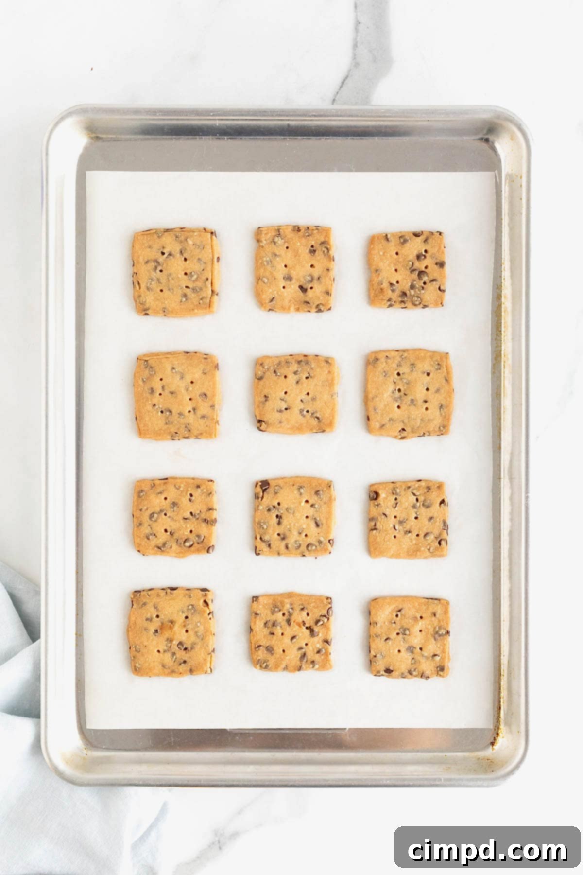 Crispy Chocolate Chip Snaps 10 A dozen freshly baked chocolate chip cookie crisps, golden and perfectly crisp, arranged on a parchment-lined aluminum baking sheet.