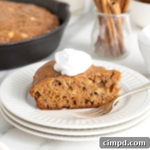 A golden slice of apple skillet cake topped with whipped cream, on a stack of plates.