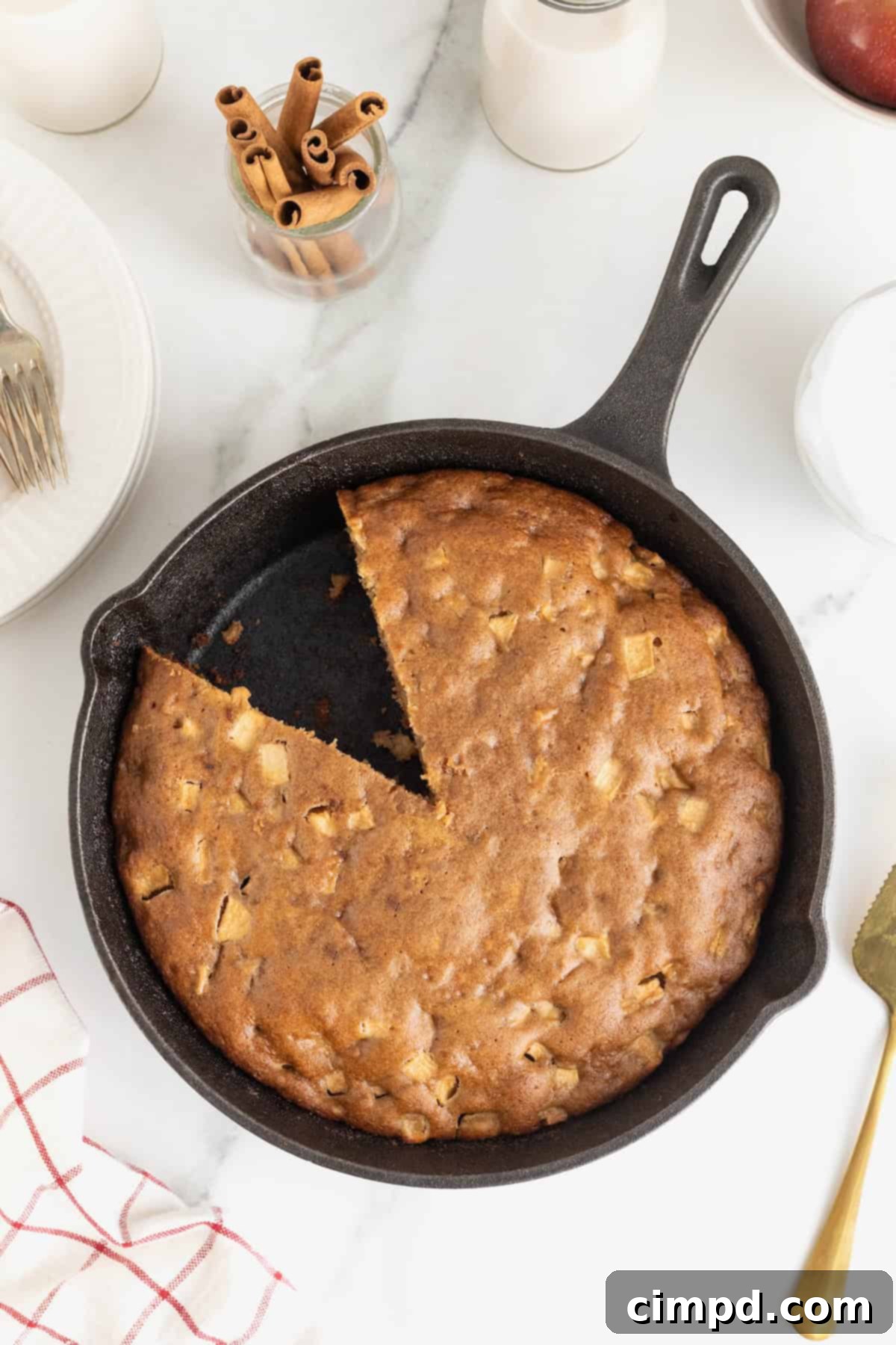A close-up shot of an apple cake baked to perfection in a classic cast iron skillet. A single slice has been removed, revealing the moist, apple-filled interior, inviting you to enjoy.