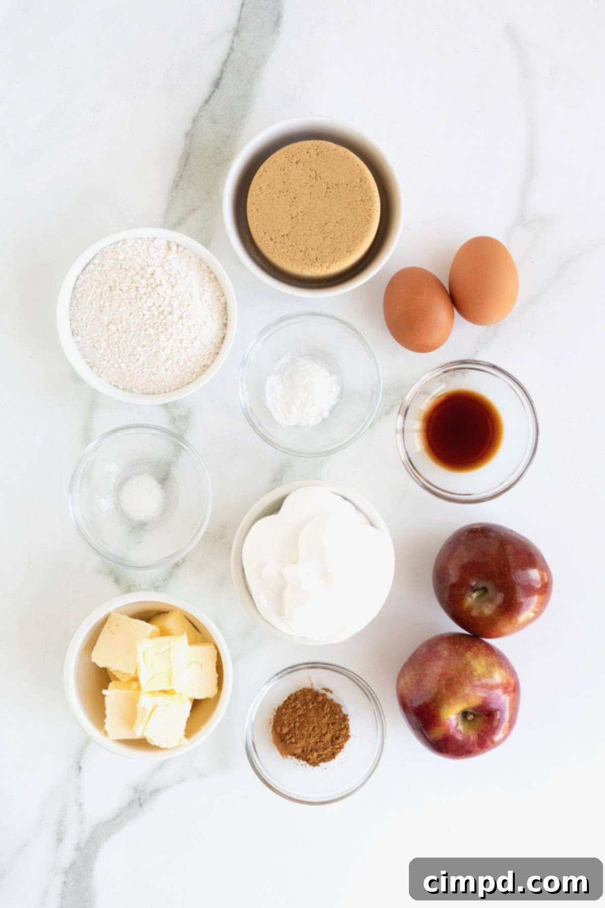 A flat lay photograph showcasing all the fresh and dry ingredients meticulously laid out to prepare the Apple Skillet Cake, including apples, butter, flour, sugar, and spices.