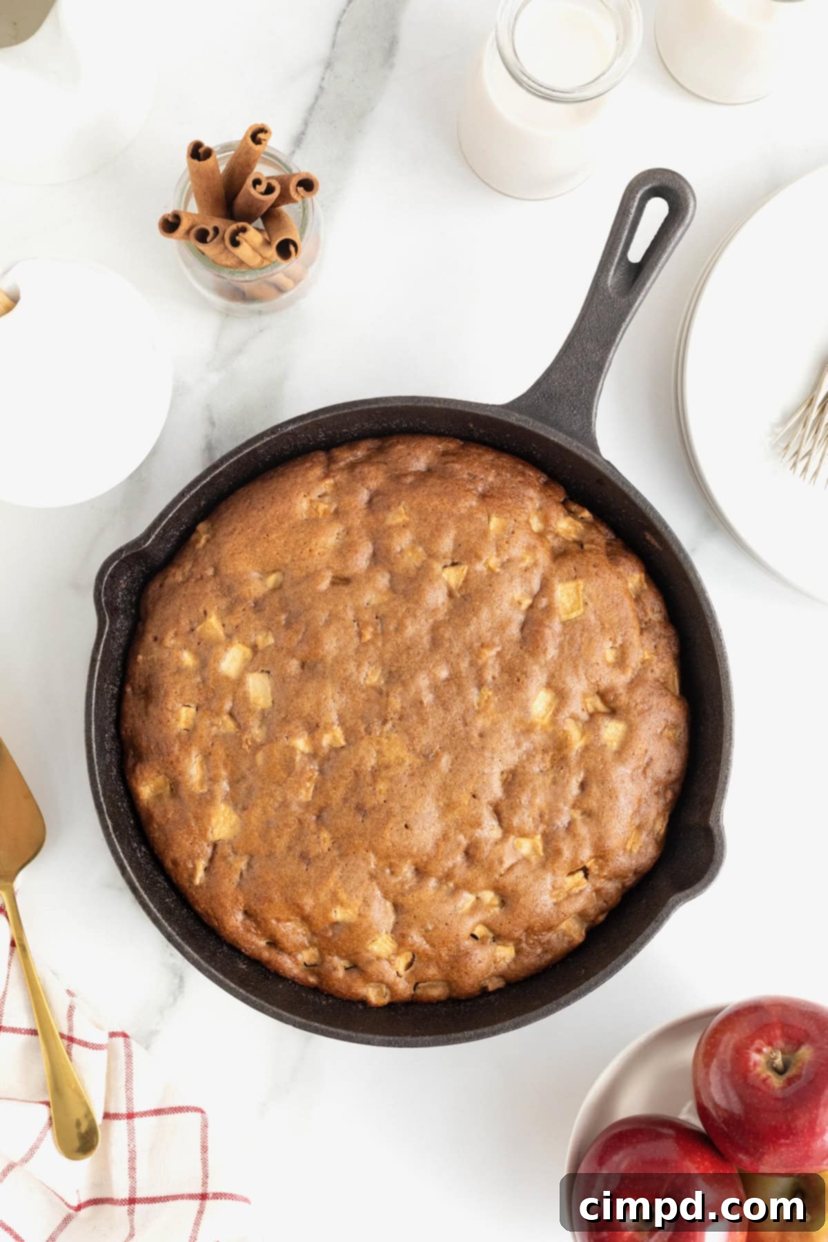 A beautifully golden-brown apple cake baked in a cast iron skillet, resting elegantly on a pristine white marble counter, ready to be served.