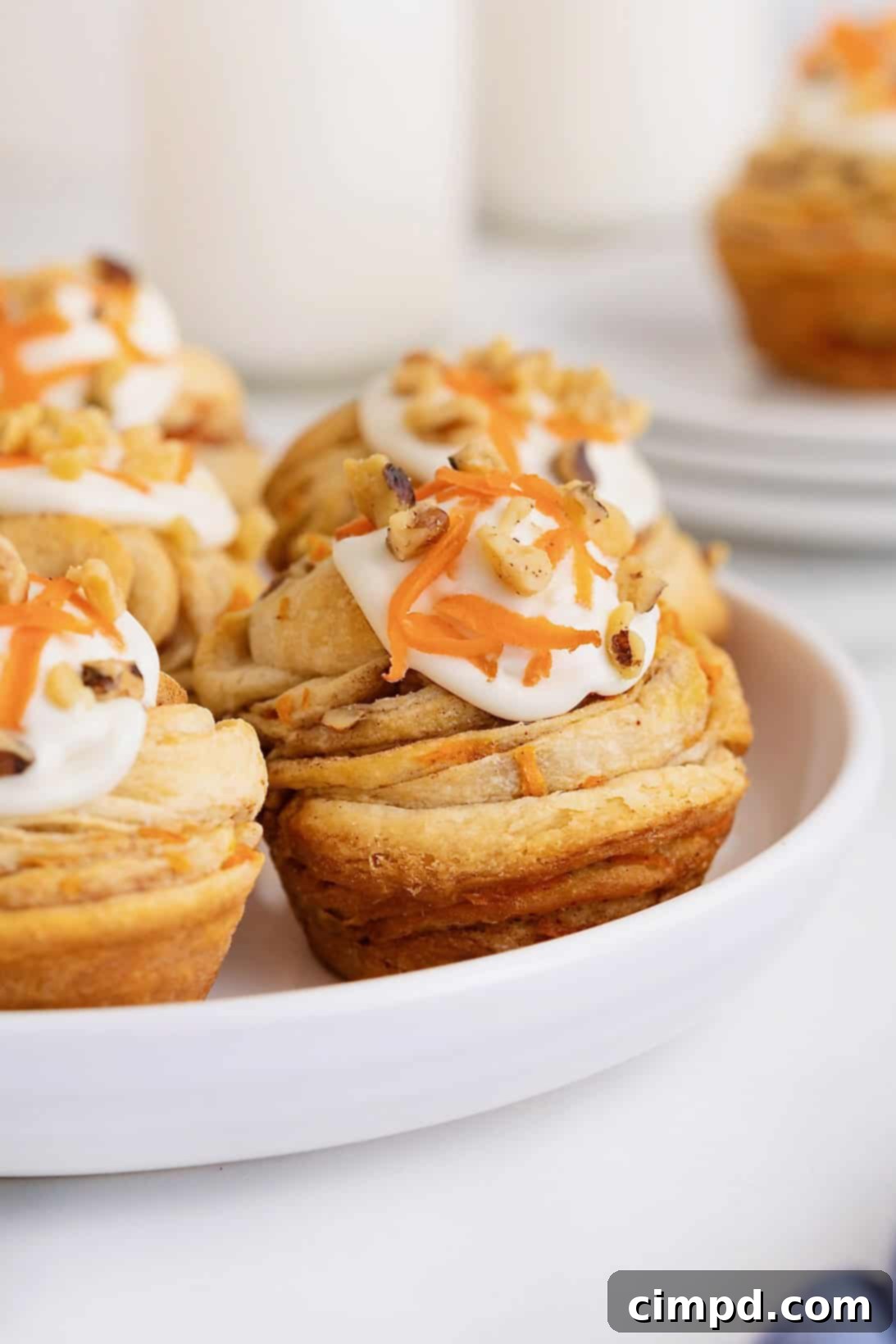 Flaky Spiced Carrot Cruffins 13 Six beautifully baked Carrot Cake Cruffins, unfrosted and displaying their golden, flaky layers, are neatly arranged on a white rimmed platter.