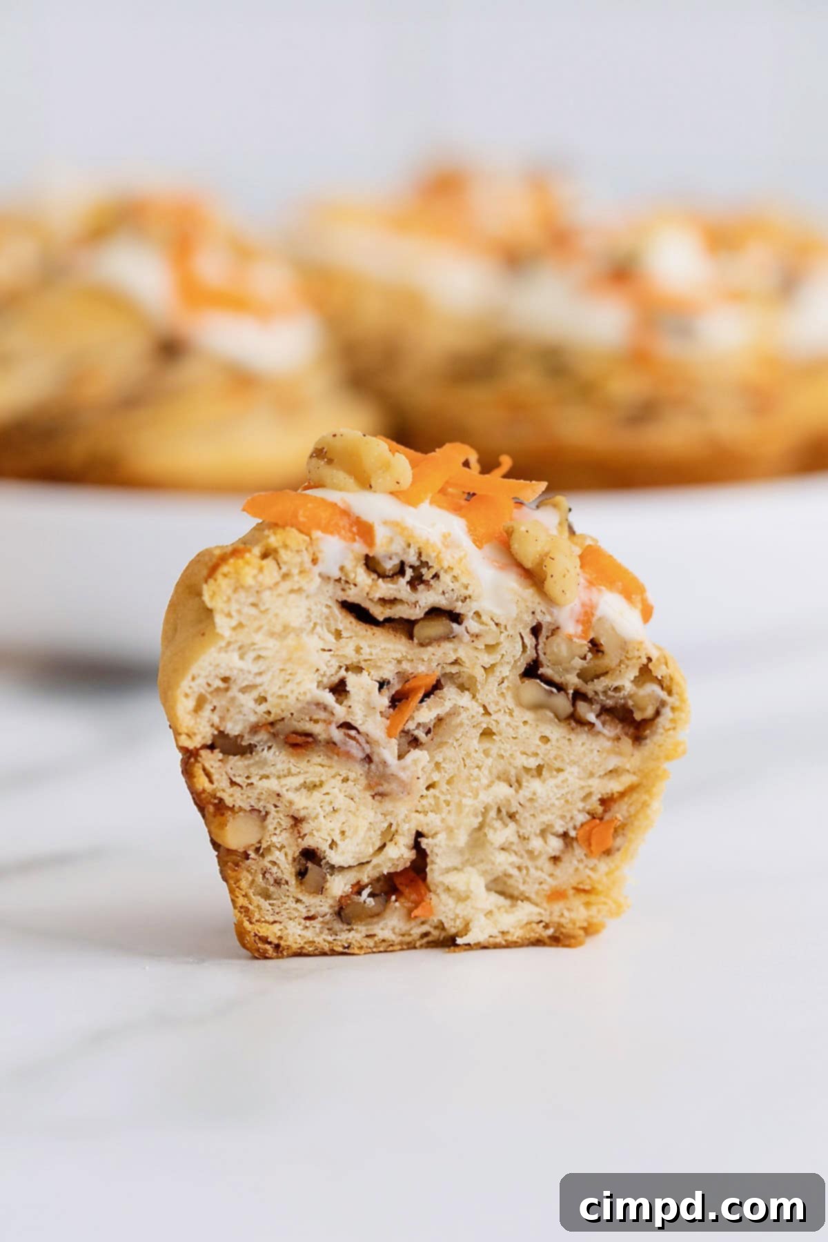 Flaky Spiced Carrot Cruffins 3 A slice of moist carrot cake with layers of cream cheese frosting rests on a white marble countertop, showcasing its rich texture and inviting appearance.