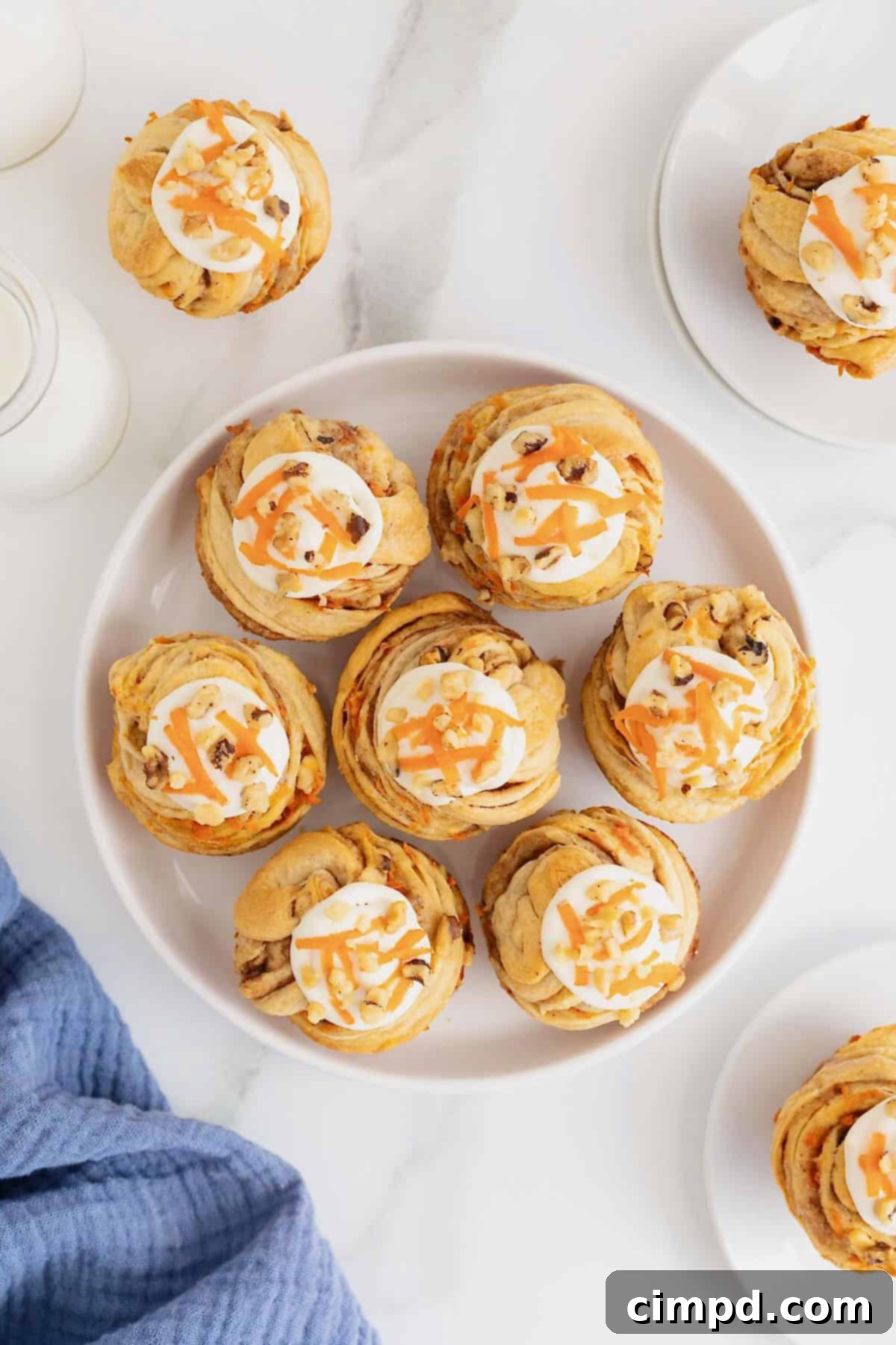 Flaky Spiced Carrot Cruffins 5 Seven frosted Carrot Cake Cruffins arranged neatly on a large, elegant white serving plate, showcasing their inviting golden color and creamy toppings.