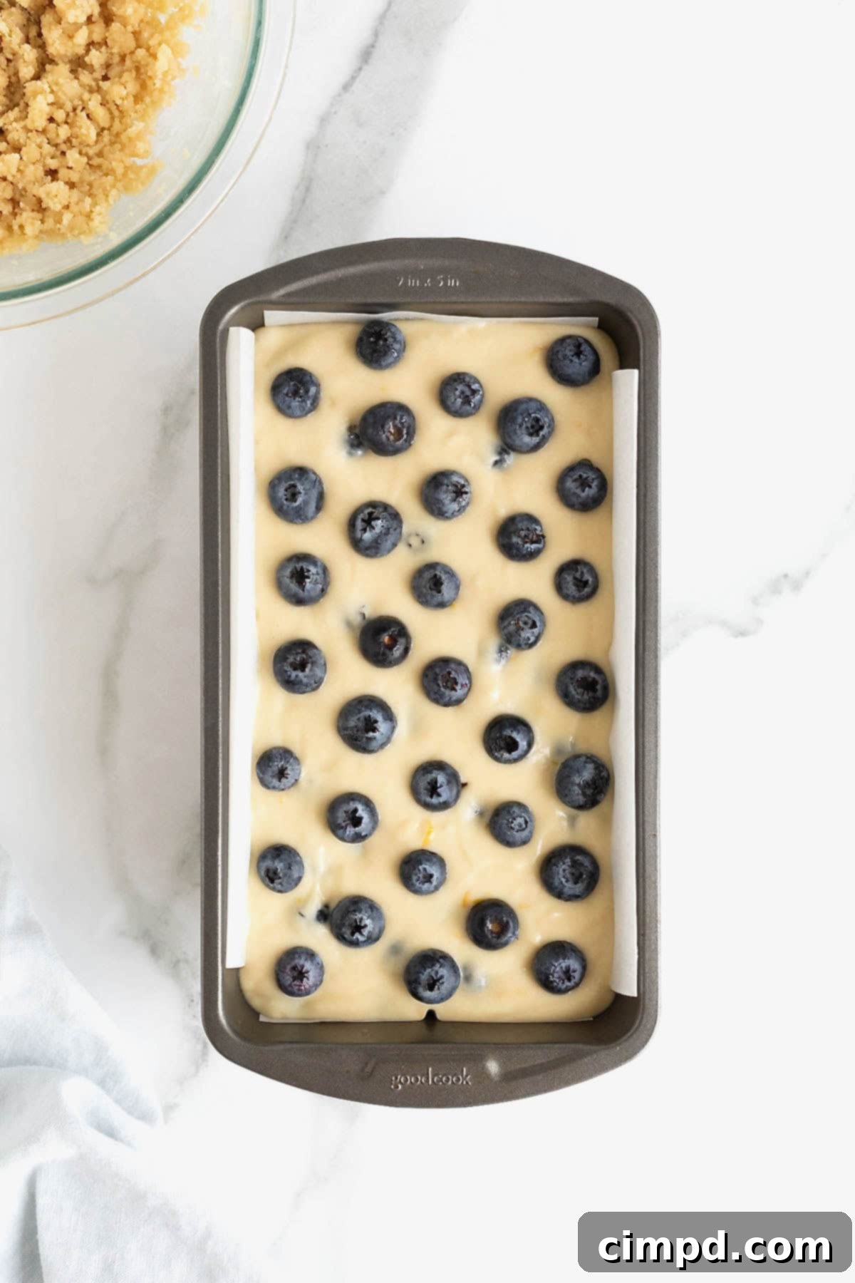 Blueberries on top of lemon blueberry bread batter in a dark aluminum loaf pan.