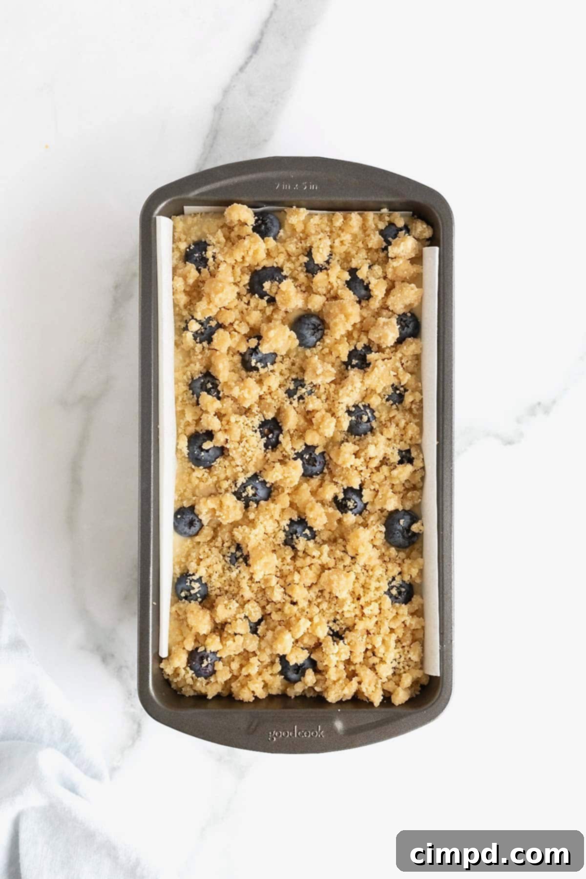 Streusel sprinkled on lemon blueberry bread batter in a loaf pan.