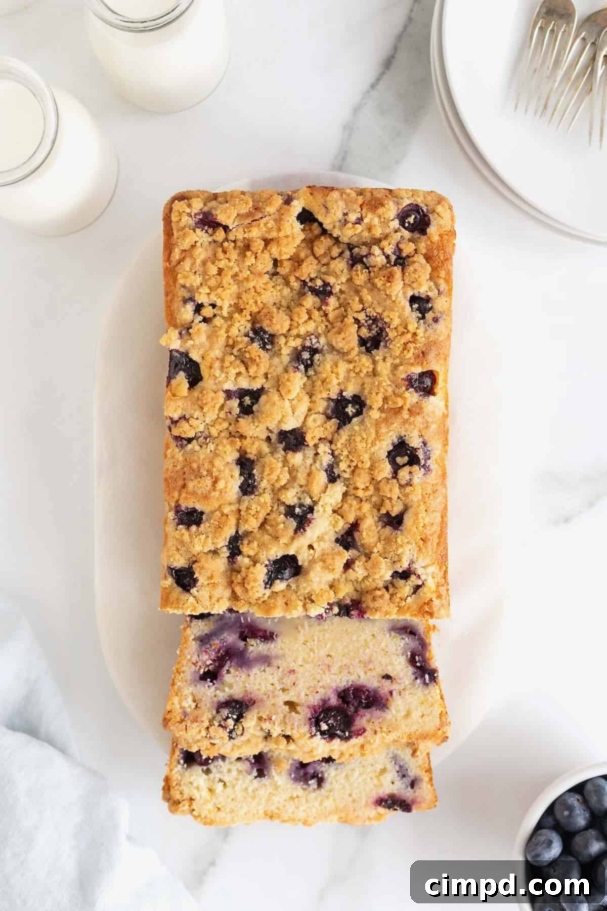 A loaf of lemon blueberry bread studded with blueberries and topped with a streusel on a whim serving platter.