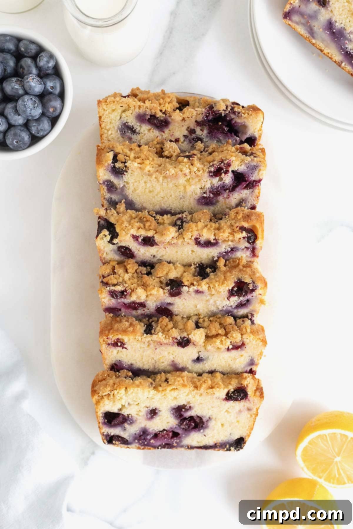 A sliced loaf of lemon blueberry bread on an oblong white cutting board.