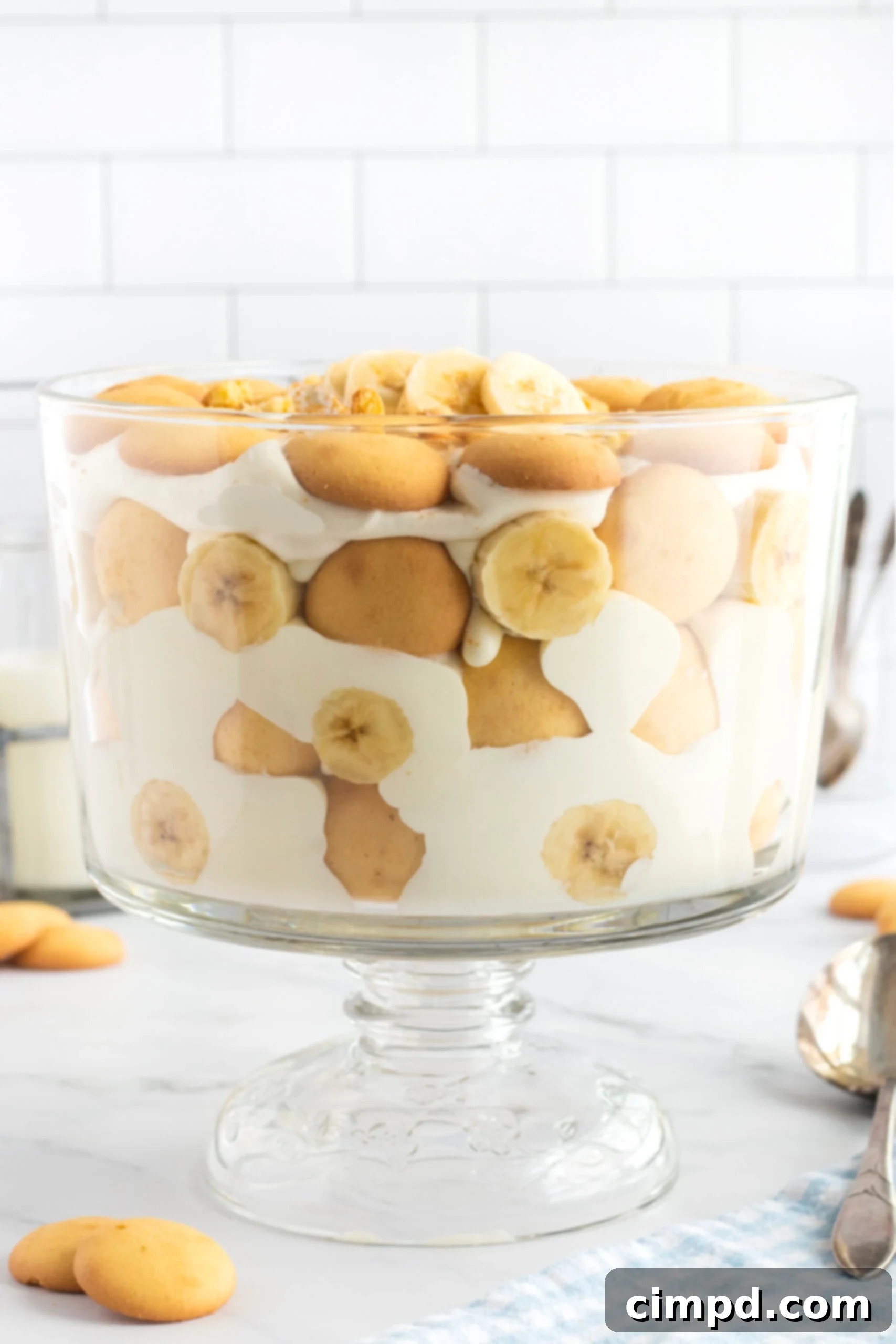 A beautifully layered glass dish of the best banana pudding, featuring golden vanilla wafers, creamy pudding, and fresh banana slices, ready to be served.
