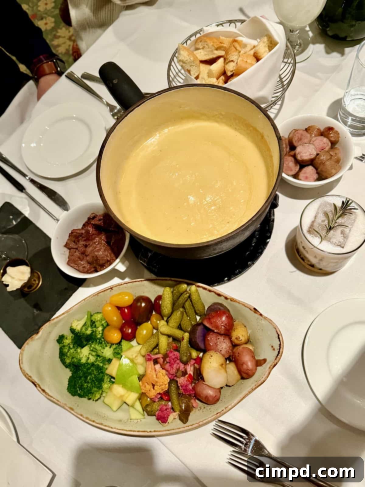 A warm pot of fondue surrounded by a plate of fresh bread, fruits, and vegetables for dipping.