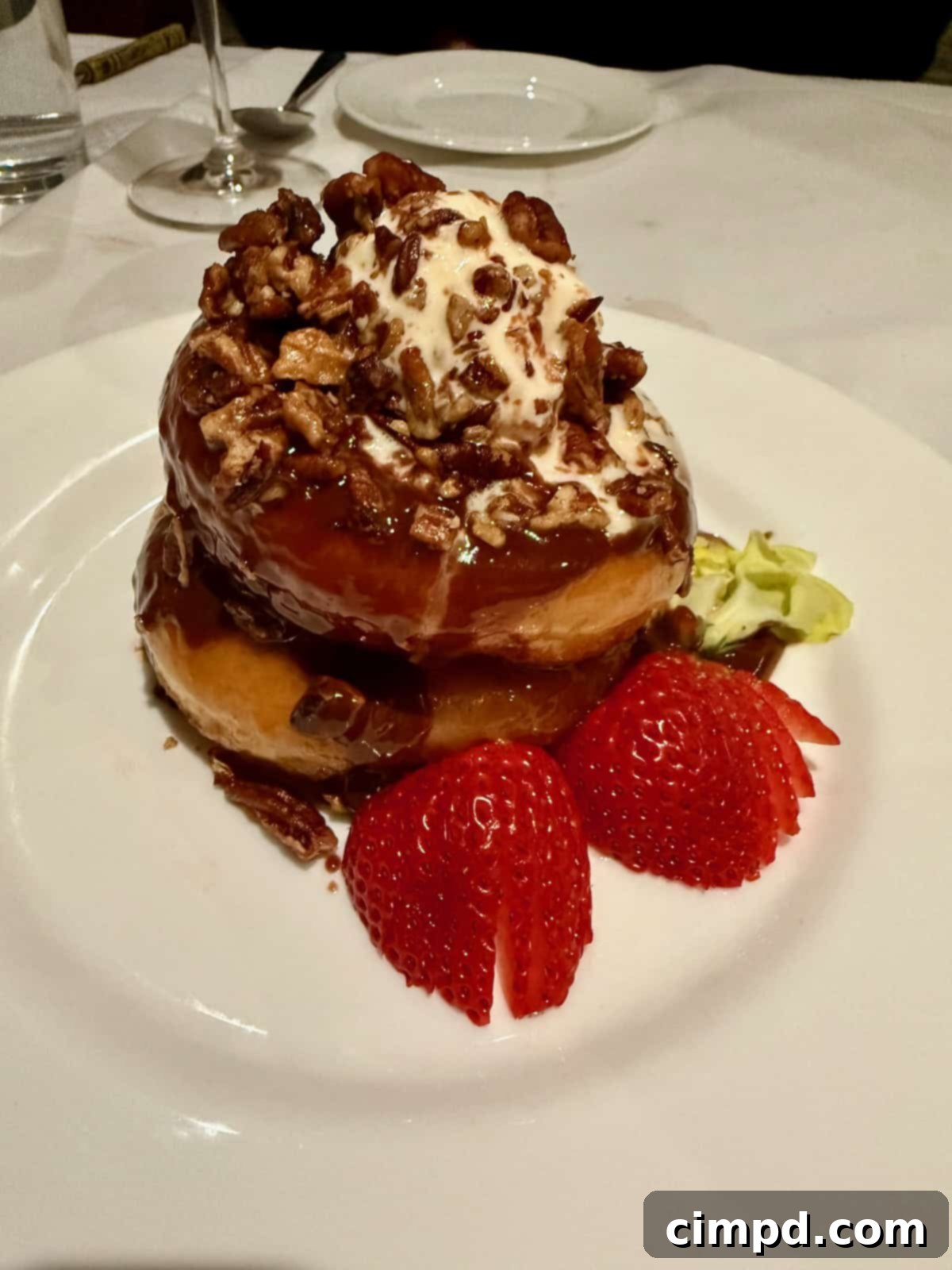A stack of warm glazed donuts elegantly garnished with fresh strawberry halves on a white plate.