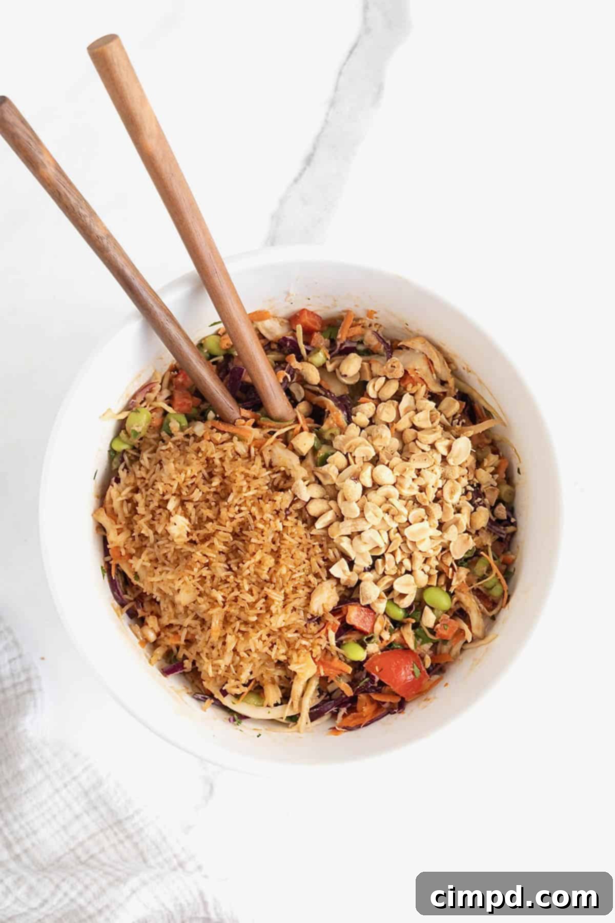 Crispy rice and chopped peanuts added to a salad in a large white bowl.