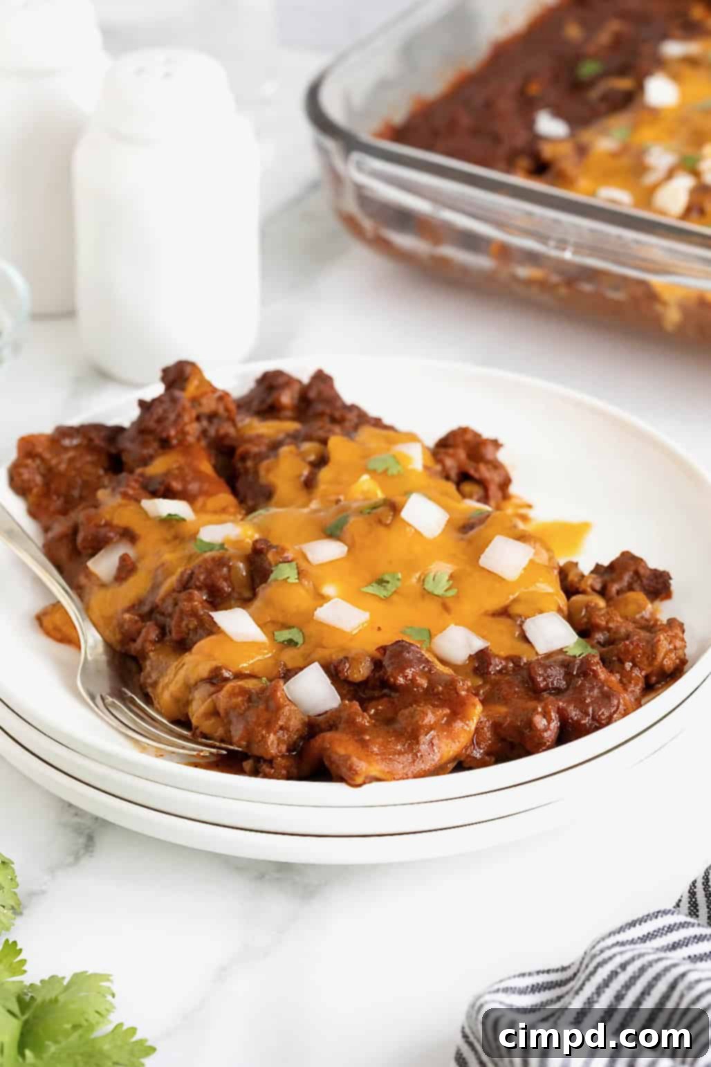 Three golden-brown Chili Con Carne Enchiladas topped with melted cheese and fresh cilantro, served on white plates.