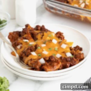 Three chili con carne enchiladas on a stack of three white plates.