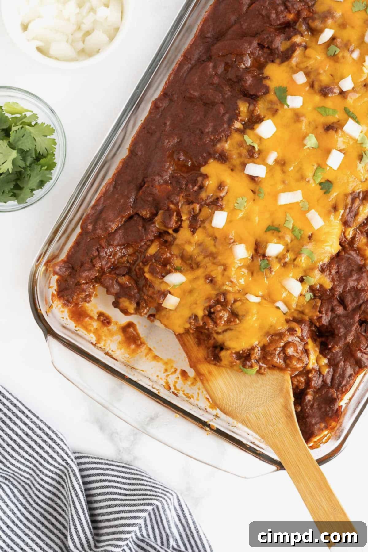 A large pyrex dish brimming with Chili Con Carne Enchiladas, topped with a rich, bubbling sauce and melted cheese.