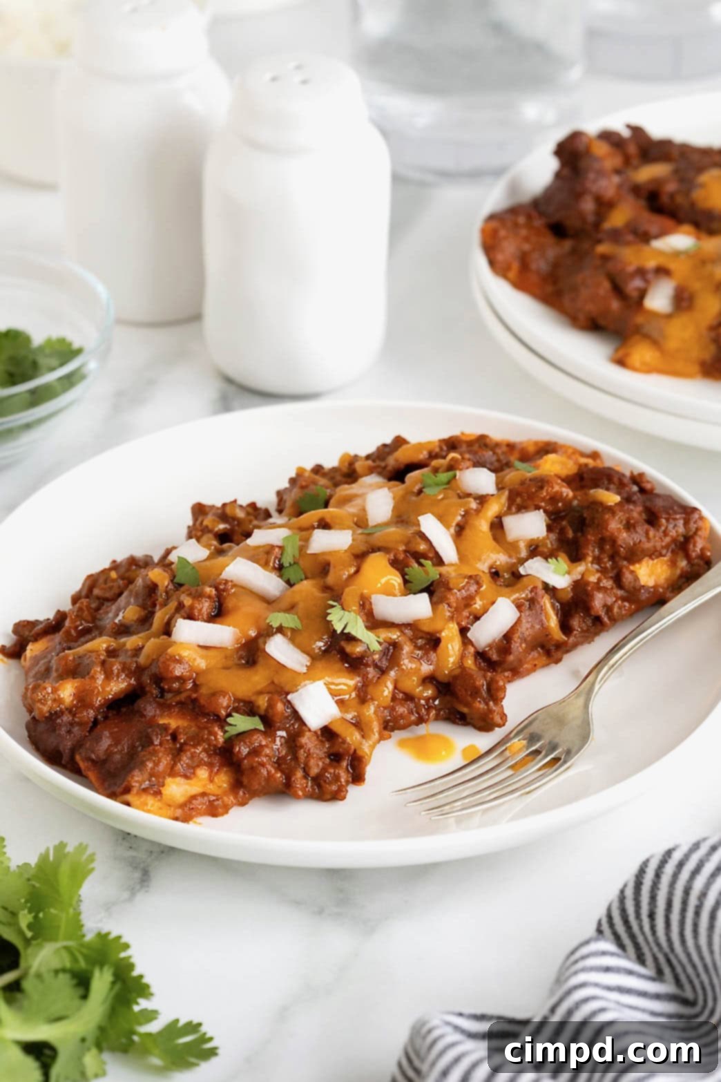 Three Chili Con Carne Enchiladas on a pristine white plate, garnished with fresh cilantro, ready to be enjoyed.