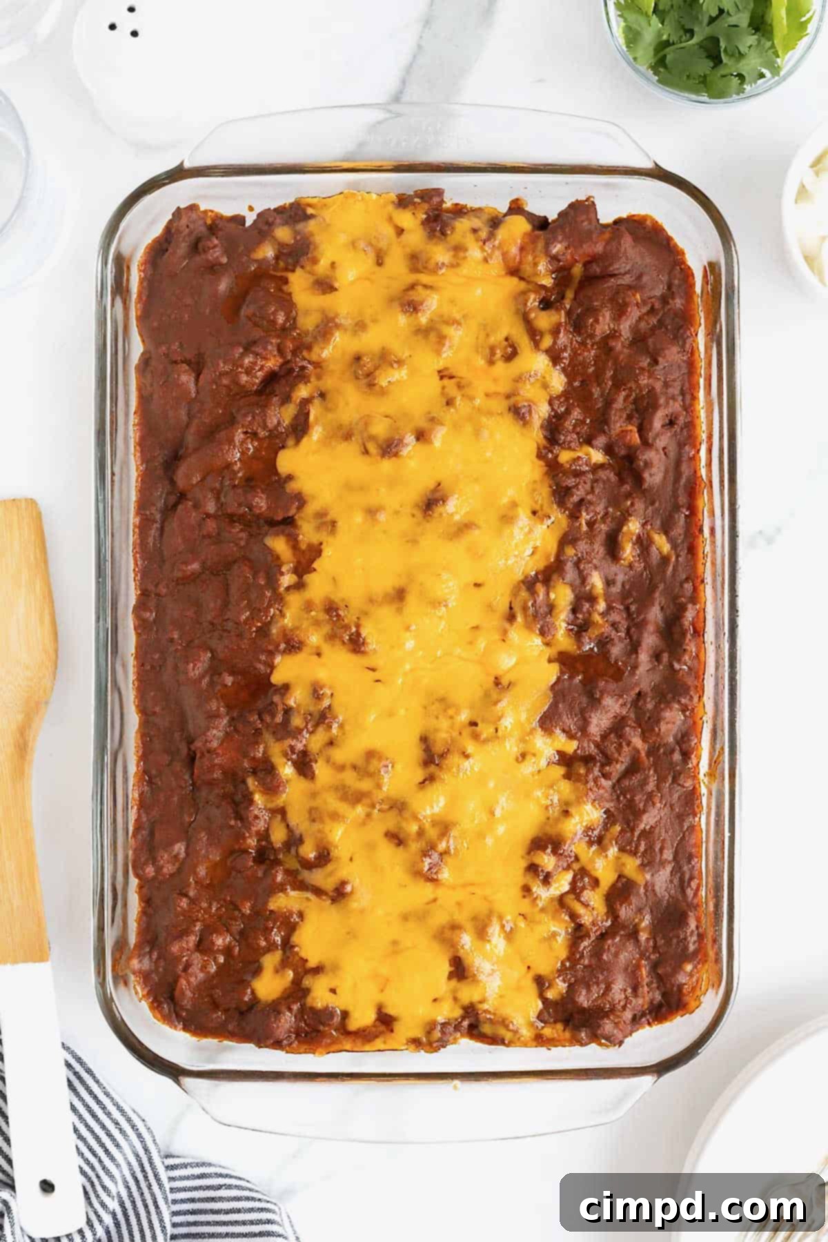 A bubbling glass baking dish of Chili Con Carne Enchiladas fresh from the oven, topped with melted cheddar cheese.
