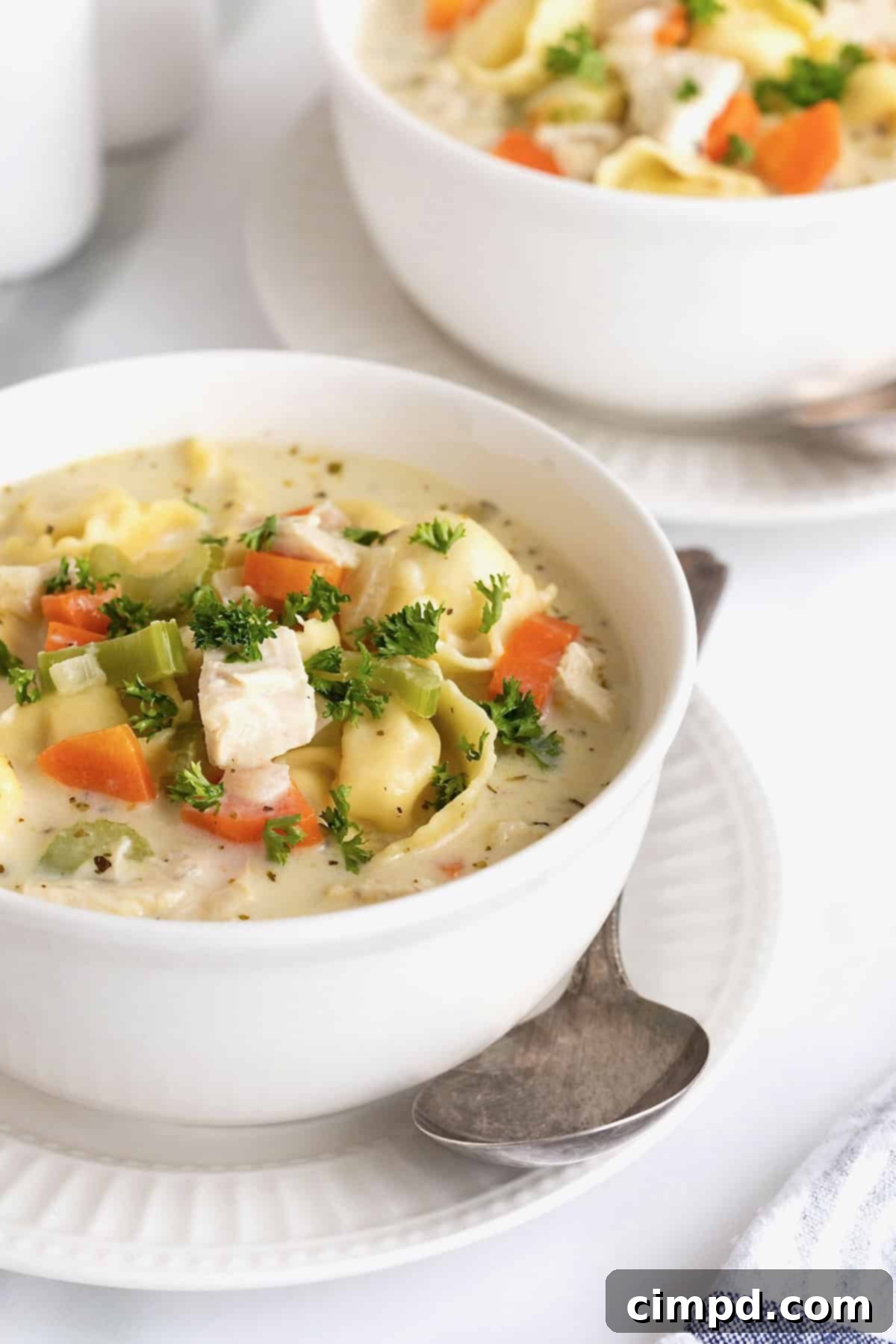 Homestyle Creamy Chicken Tortellini Soup 3 Two bowls of creamy chicken tortellini soup on white fluted plates.