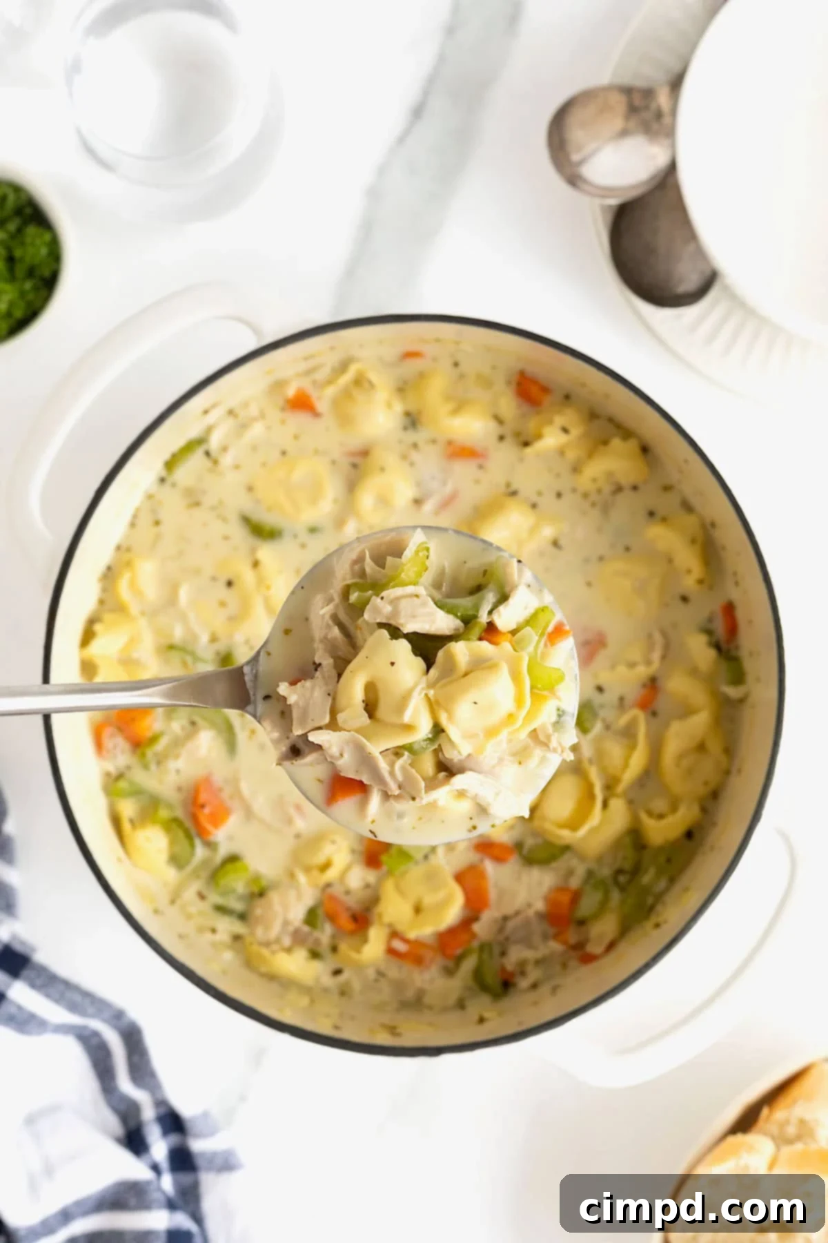 Homestyle Creamy Chicken Tortellini Soup 4 A ladle lifting tortellini soup out of a white dutch oven.