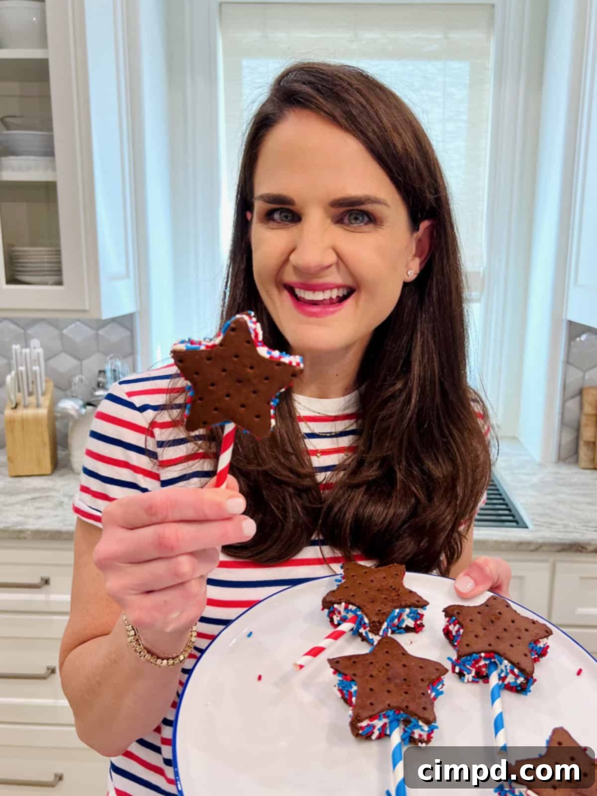 Simple Star-Spangled Bites 8 Maegan Brown, wearing a festive red, white, and blue striped shirt, proudly holds a star-shaped ice cream sandwich on a striped straw, adorned with sprinkles.