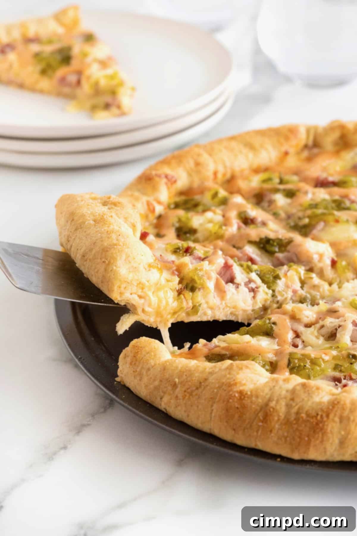 A hand lifting a slice of cheesy Reuben pizza, revealing the perfectly baked stuffed crust.