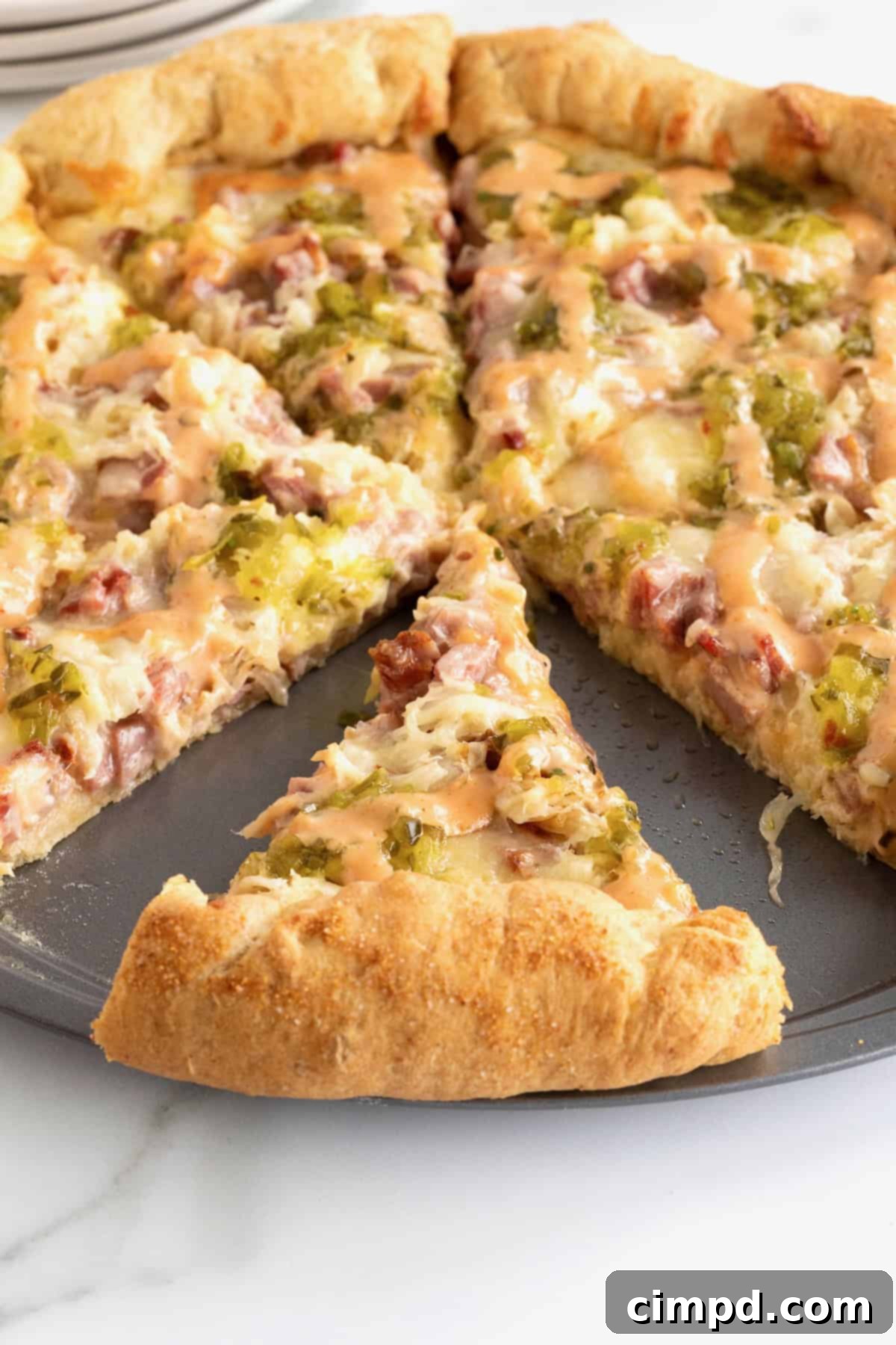 A close-up shot of a Reuben pizza with a slice removed, highlighting the layers of toppings and the golden-brown crust.