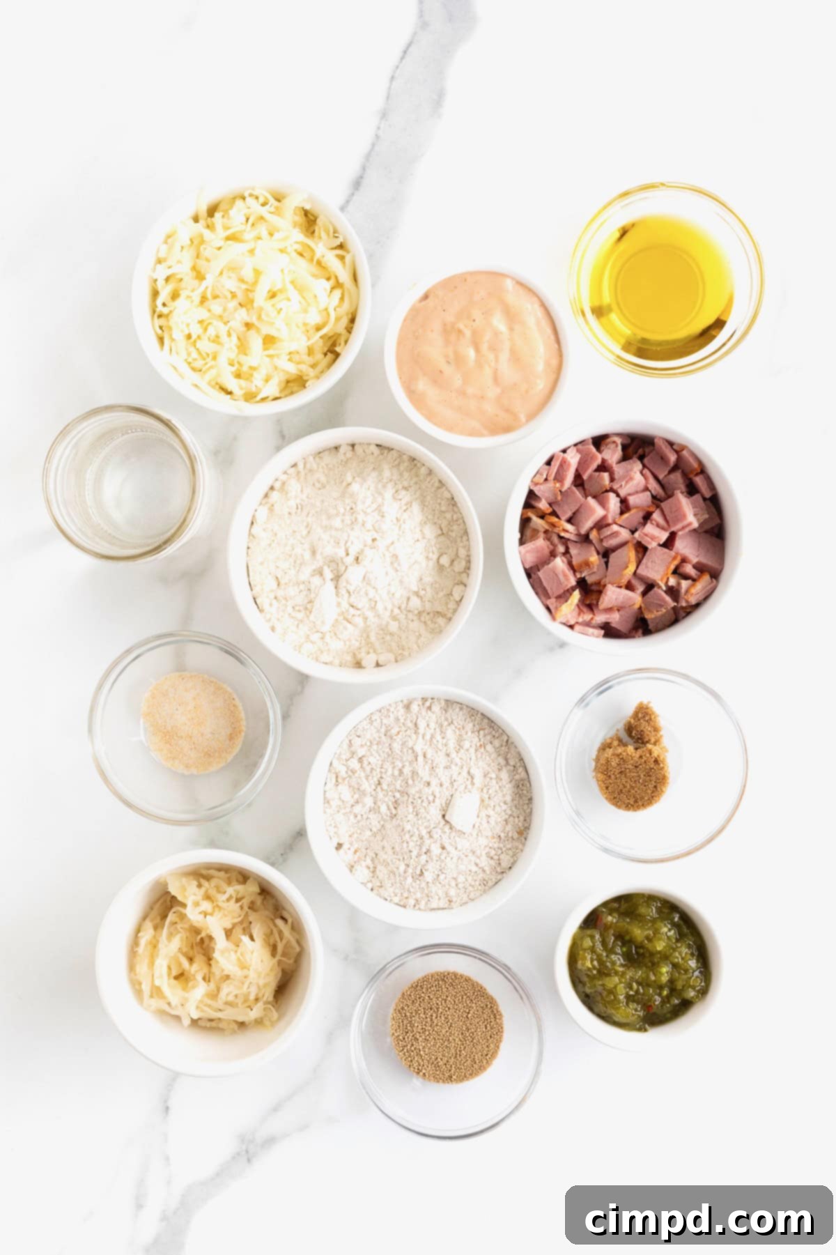 Small glass dishes filled with ingredients for Reuben Pizza, neatly arranged on a white marble counter, ready for preparation.