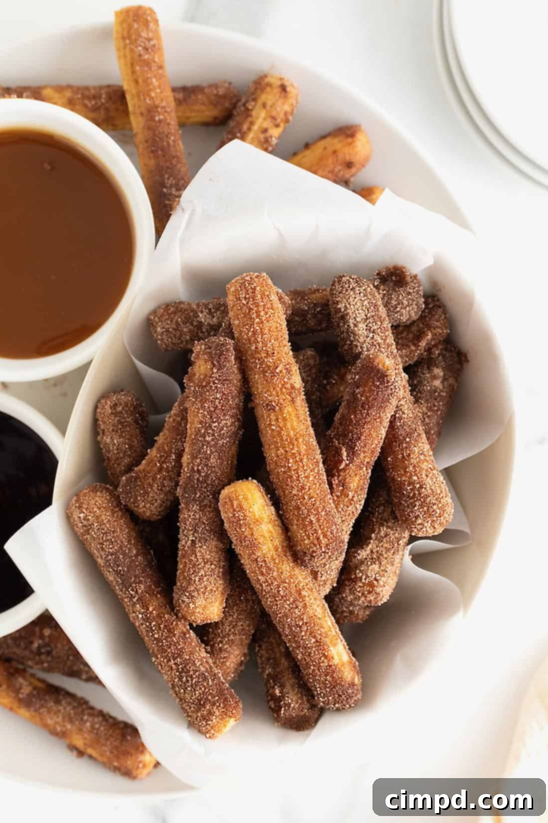 Guilt-Free Baked Churros 2 A parchment lined bowl of baked churros next to dipping sauces in white bowls.