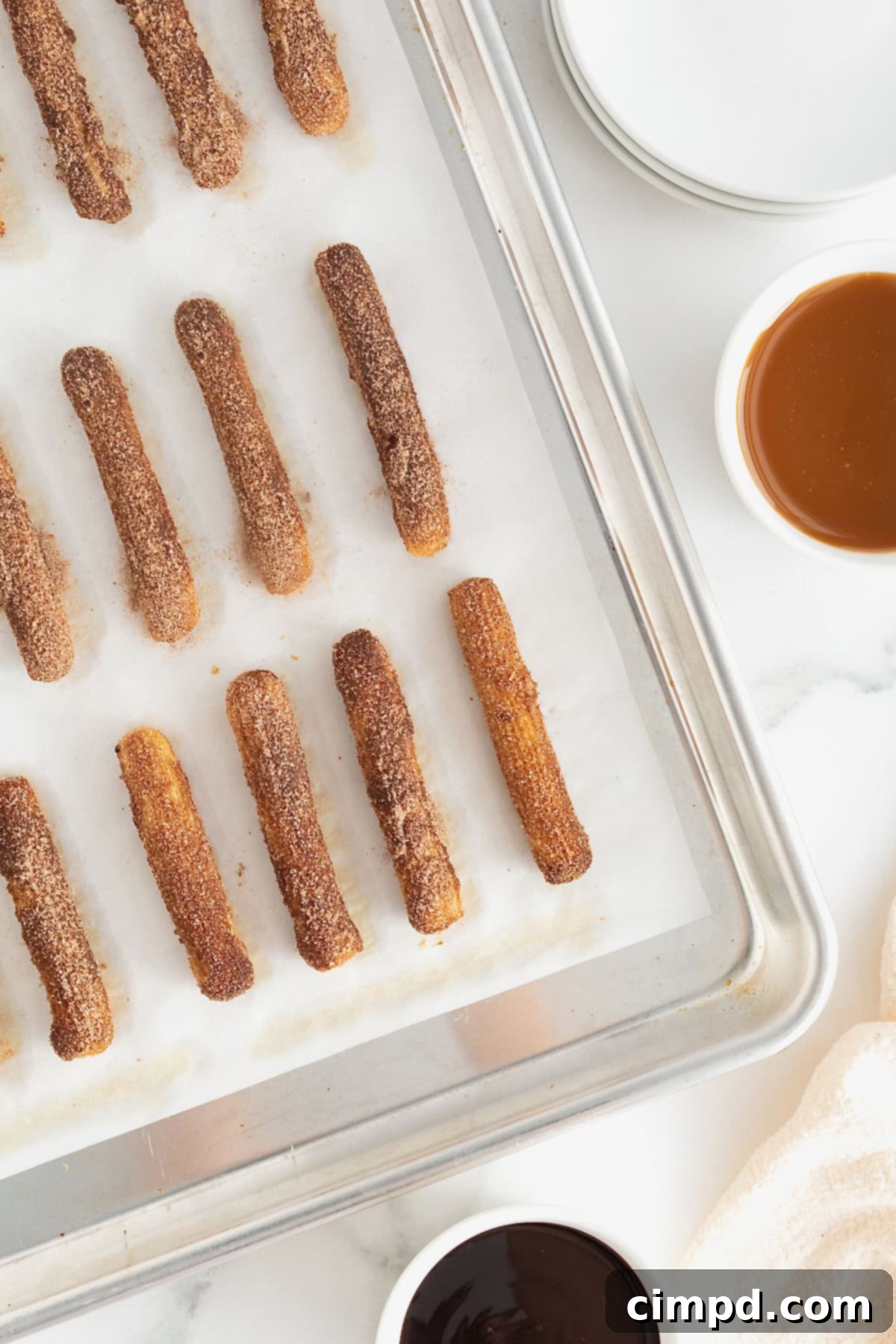 Guilt-Free Baked Churros 12 Homemade baked churros on a parchment lined aluminum baking sheet.