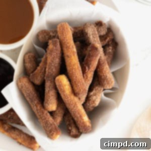 Guilt-Free Baked Churros 14 A parchment lined bowl of baked churros next to dipping sauces in white bowls.